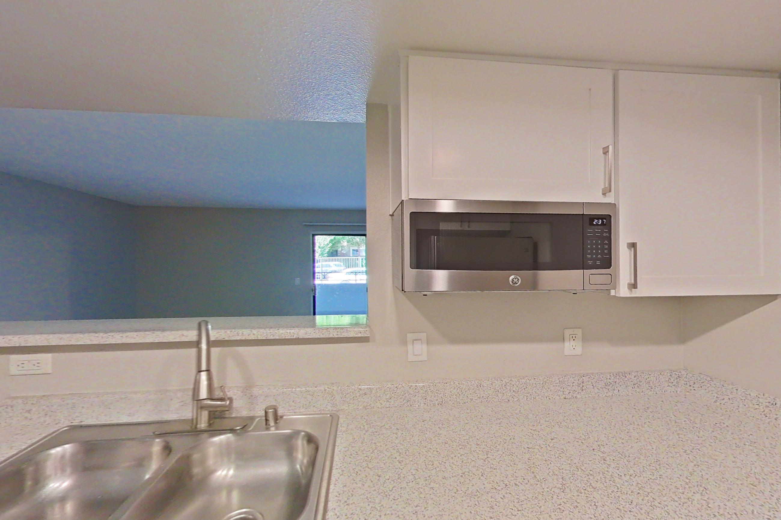 Kitchen with dishwasher, electric range, in-unit laundry, light countertops, light stone countertops, light wood-finish flooring, oven/range, refrigerator, and stainless steel appliances, Apartment 02 at Avana Rancho Cucamonga