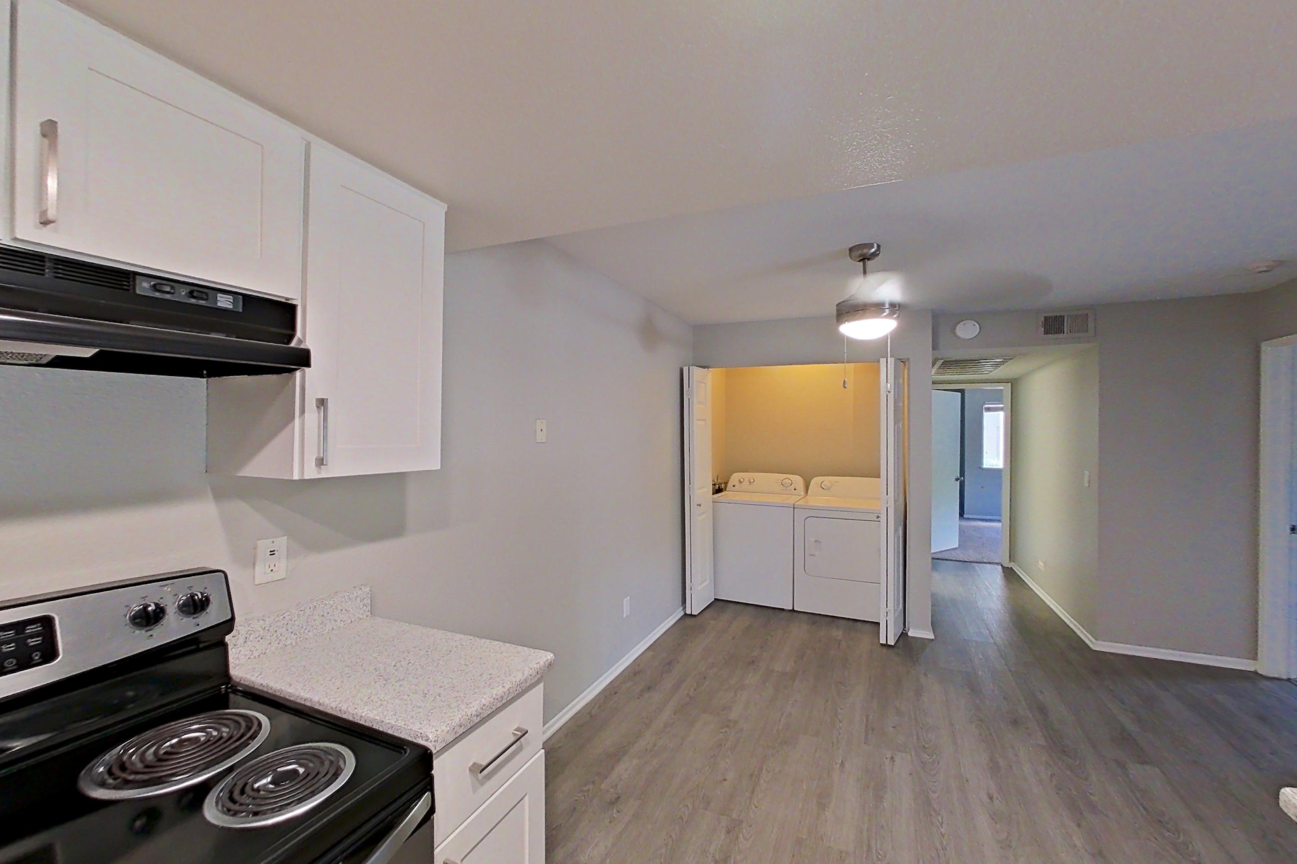 Kitchen with dishwasher, electric range, in-unit laundry, light countertops, light stone countertops, light wood-finish flooring, oven/range, refrigerator, and stainless steel appliances, Apartment 02 at Avana Rancho Cucamonga
