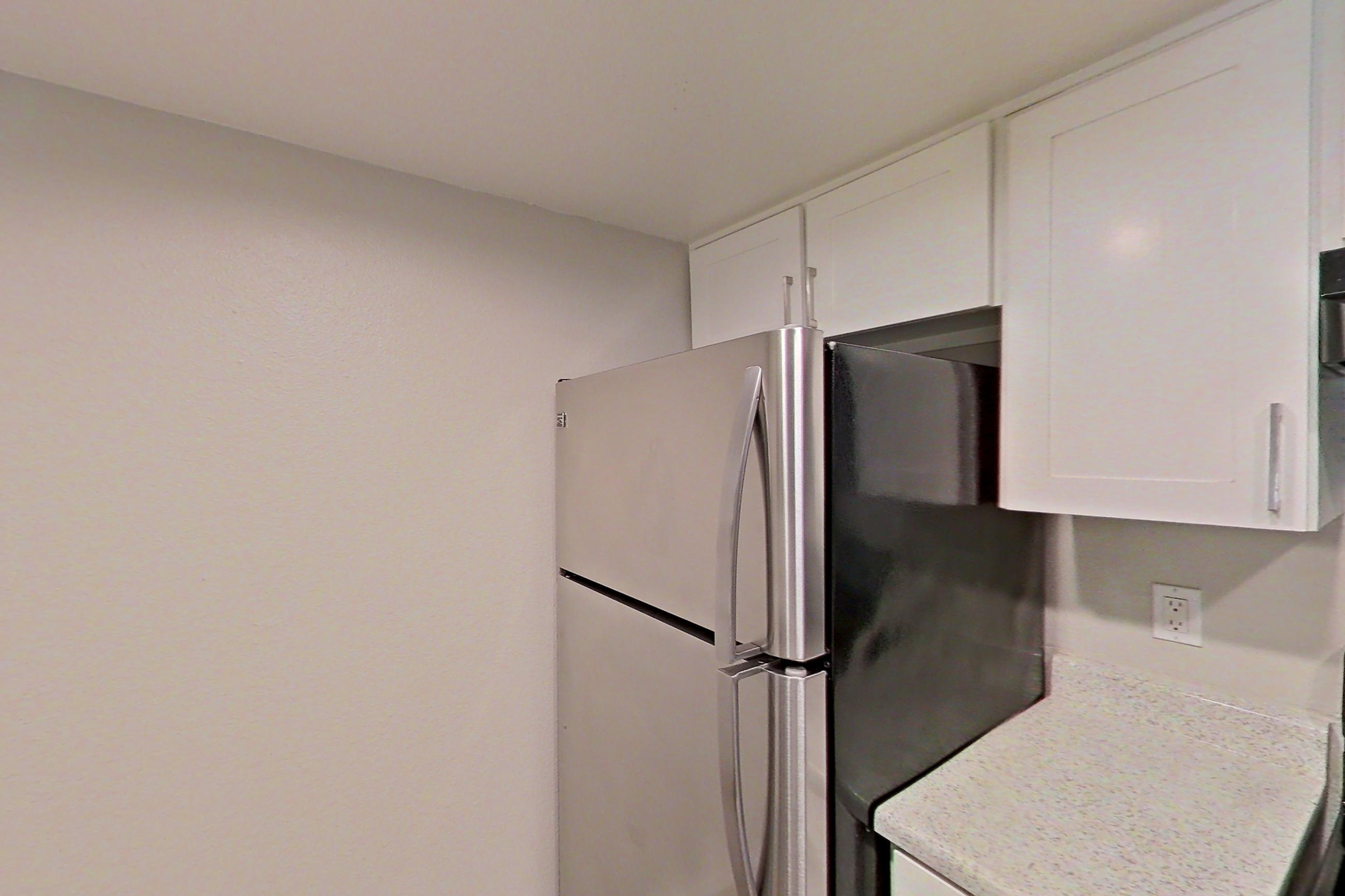 Kitchen with dishwasher, electric range, in-unit laundry, light countertops, light stone countertops, light wood-finish flooring, oven/range, refrigerator, and stainless steel appliances, Apartment 02 at Avana Rancho Cucamonga