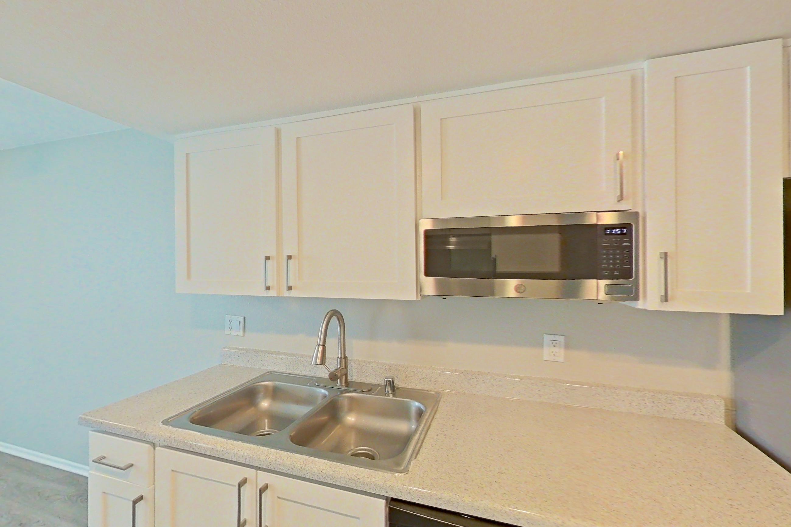 Kitchen with dishwasher, electric range, light countertops, light stone countertops, light wood-finish flooring, microwave, oven/range, range hood, refrigerator, and stainless steel appliances, Apartment 09 at Avana Rancho Cucamonga