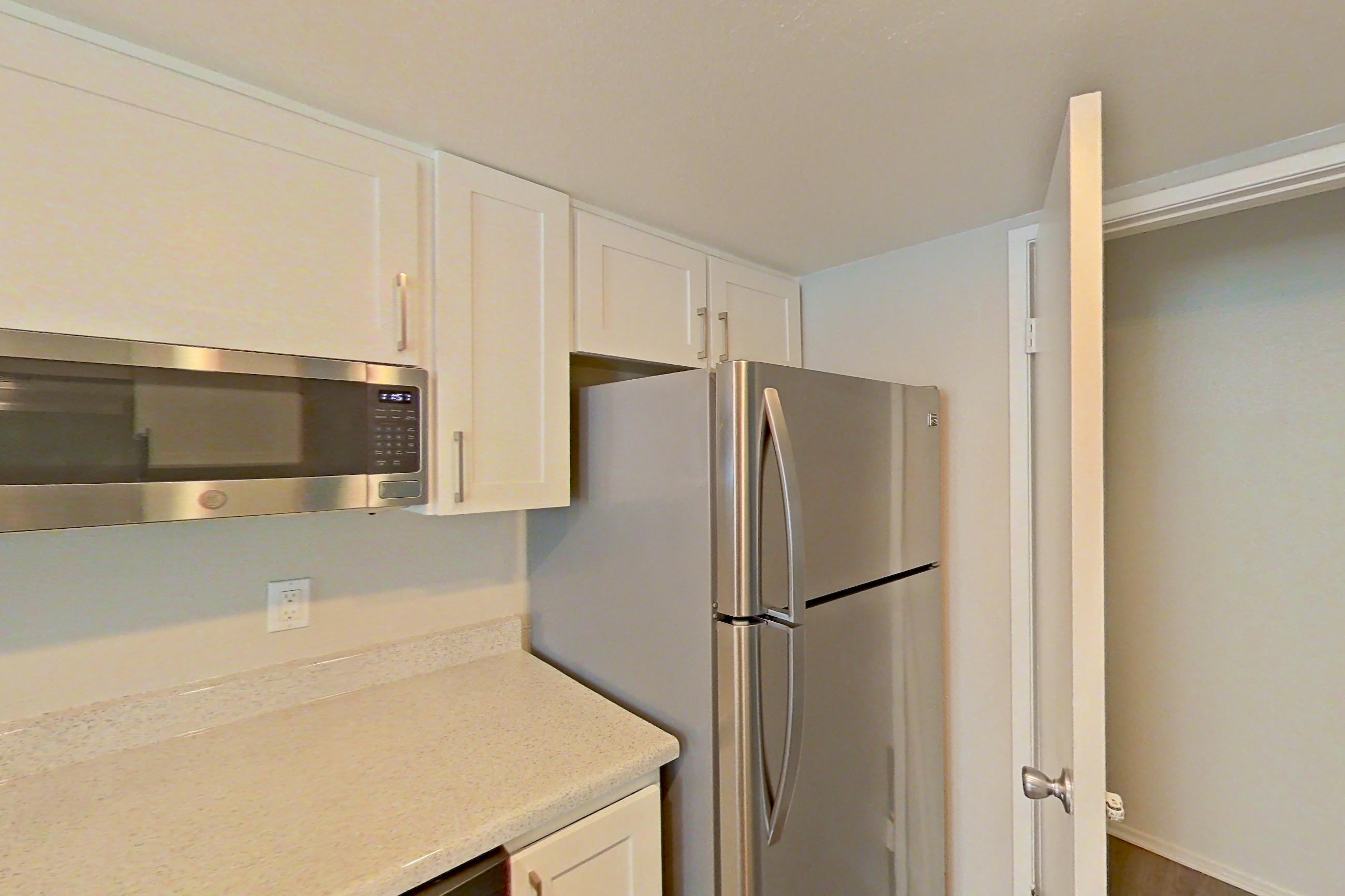 Kitchen with dishwasher, electric range, light countertops, light stone countertops, light wood-finish flooring, microwave, oven/range, range hood, refrigerator, and stainless steel appliances, Apartment 09 at Avana Rancho Cucamonga