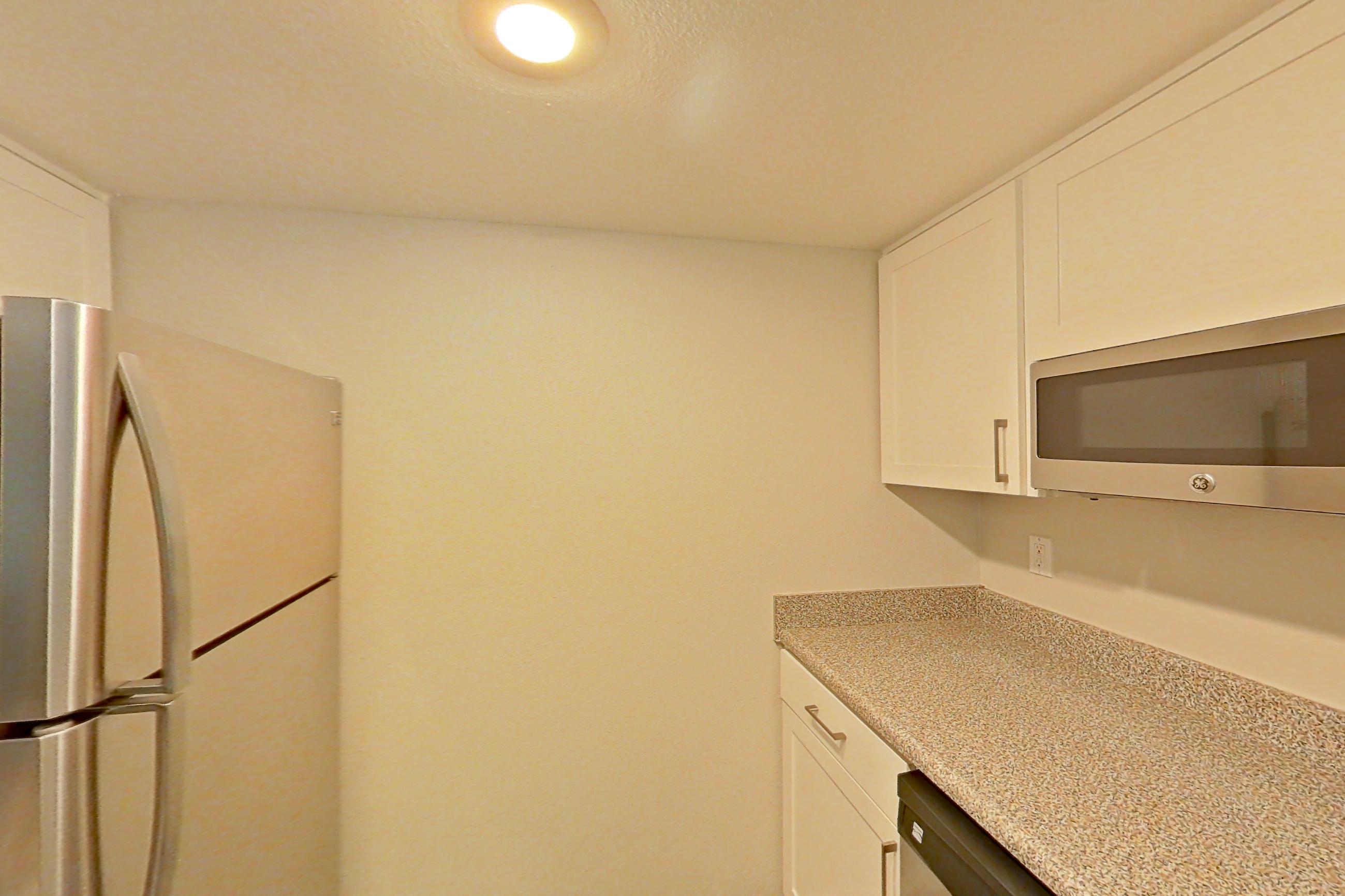 Kitchen with electric range, light countertops, light wood-finish flooring, microwave, oven/range, range hood, refrigerator, and stainless steel appliances, Apartment 05 at Avana Rancho Cucamonga