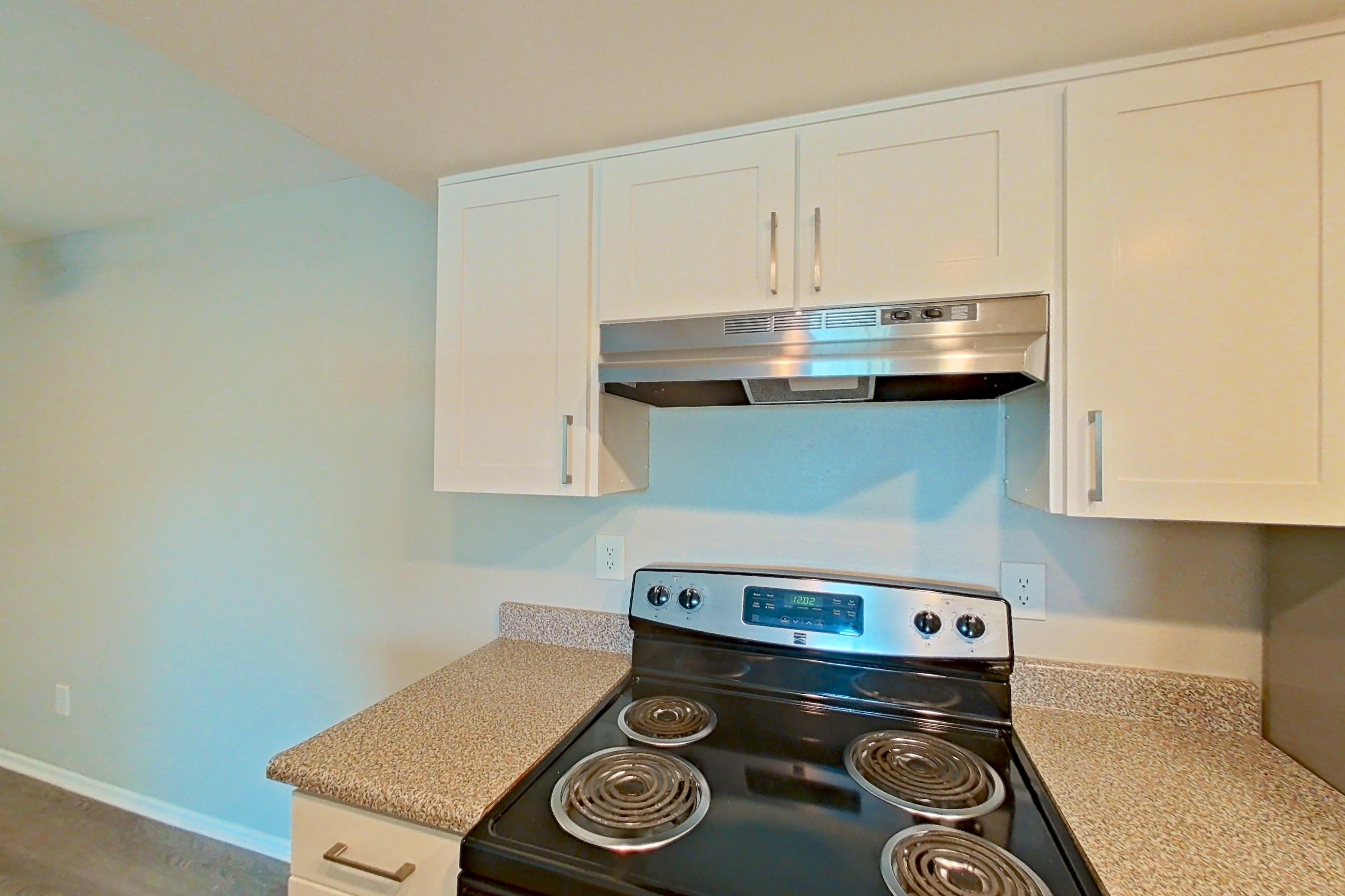 Kitchen with electric range, light countertops, light wood-finish flooring, microwave, oven/range, range hood, refrigerator, and stainless steel appliances, Apartment 05 at Avana Rancho Cucamonga