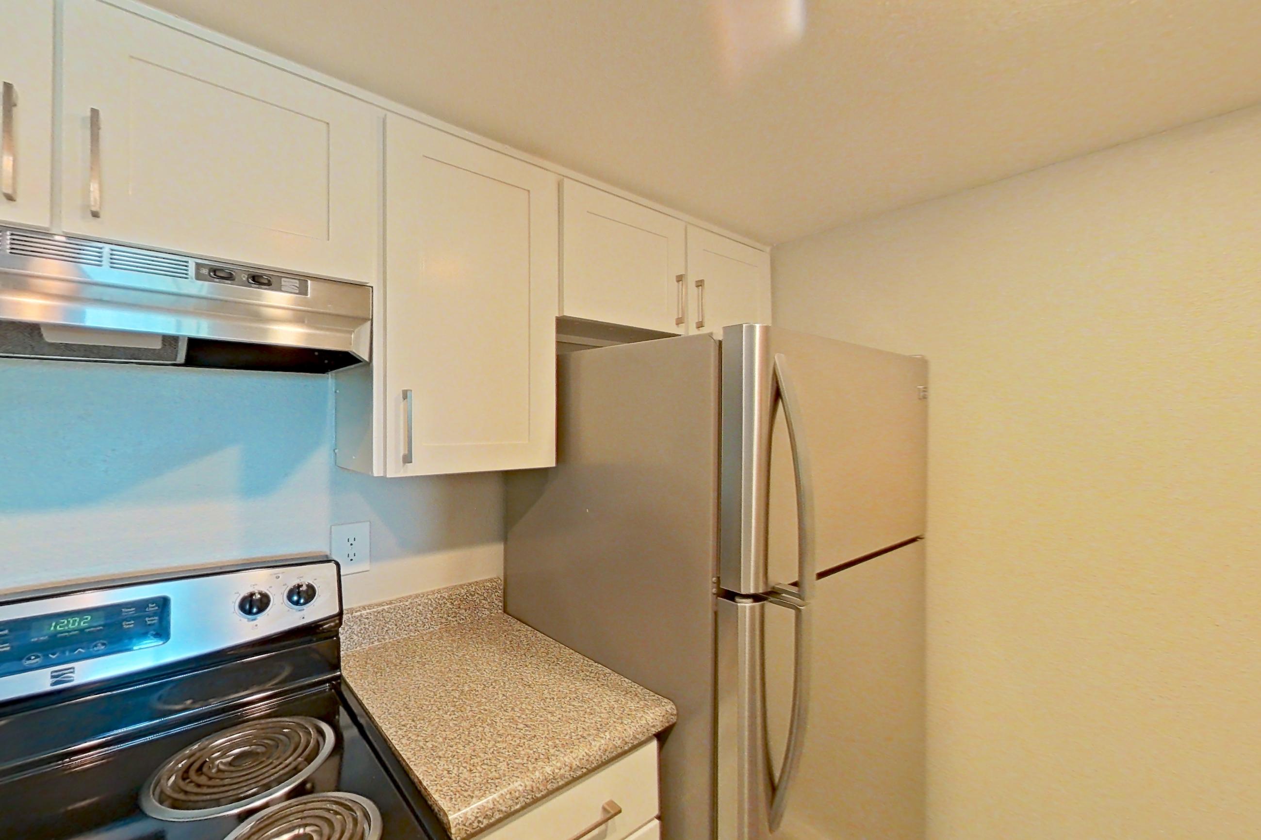 Kitchen with electric range, light countertops, light wood-finish flooring, microwave, oven/range, range hood, refrigerator, and stainless steel appliances, Apartment 05 at Avana Rancho Cucamonga