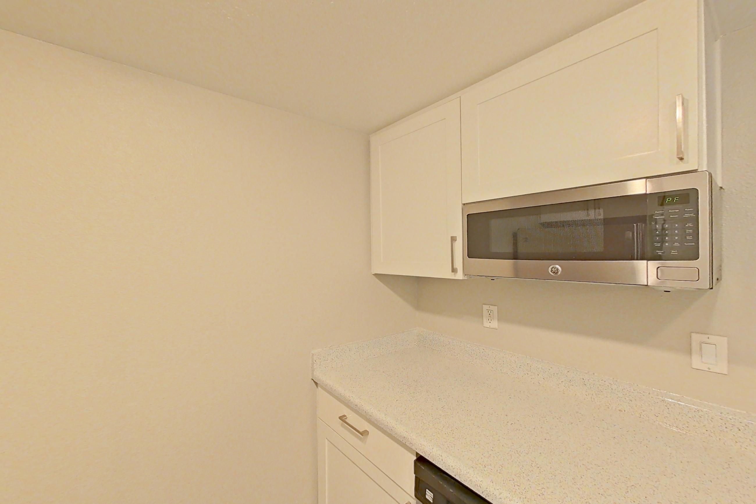 Kitchen with dishwasher, electric range, light countertops, light stone countertops, light wood-finish flooring, oven/range, range hood, refrigerator, and stainless steel appliances, Apartment 05 at Avana Rancho Cucamonga