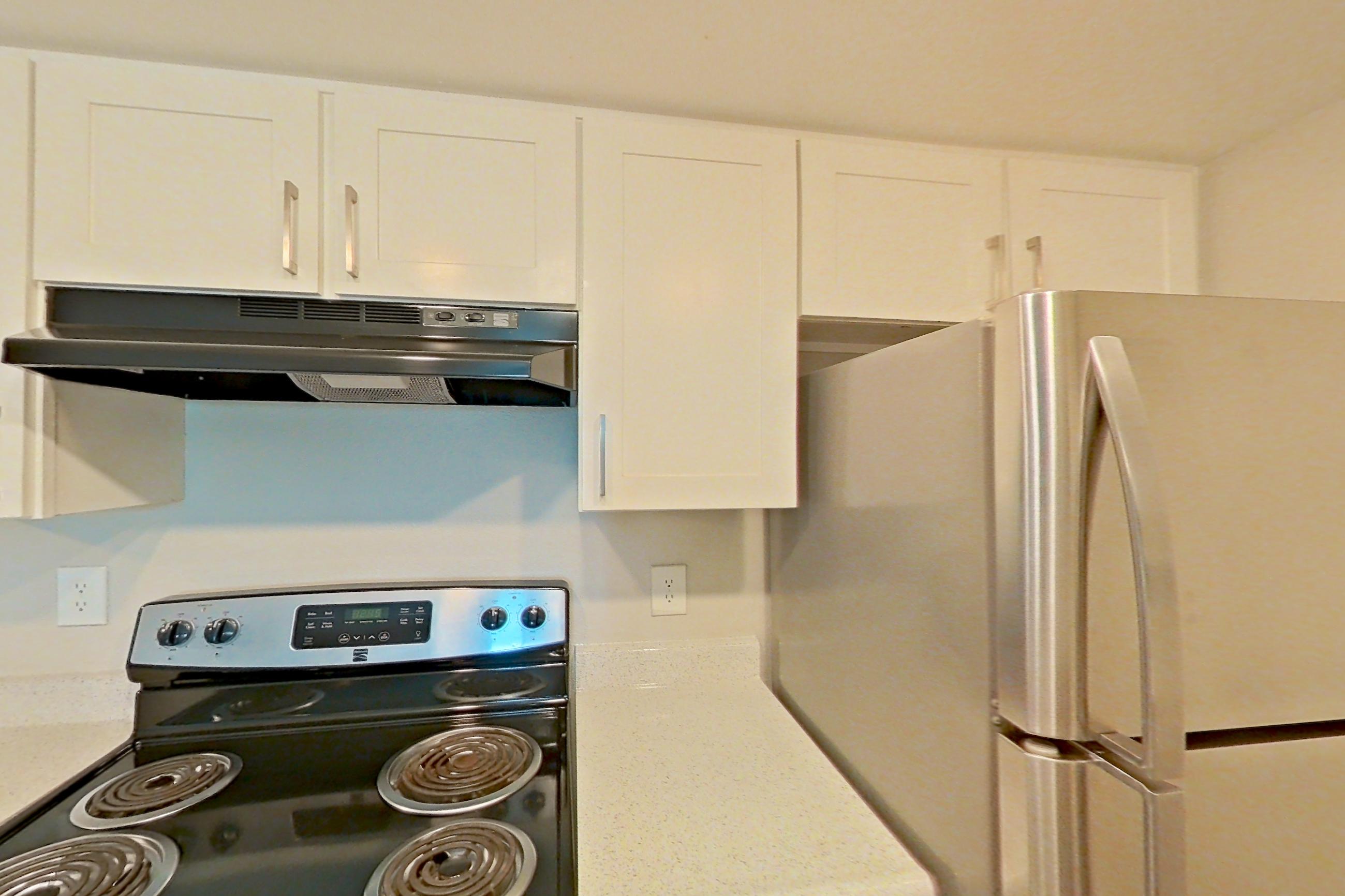 Kitchen with dishwasher, electric range, light countertops, light stone countertops, light wood-finish flooring, oven/range, range hood, refrigerator, and stainless steel appliances, Apartment 05 at Avana Rancho Cucamonga