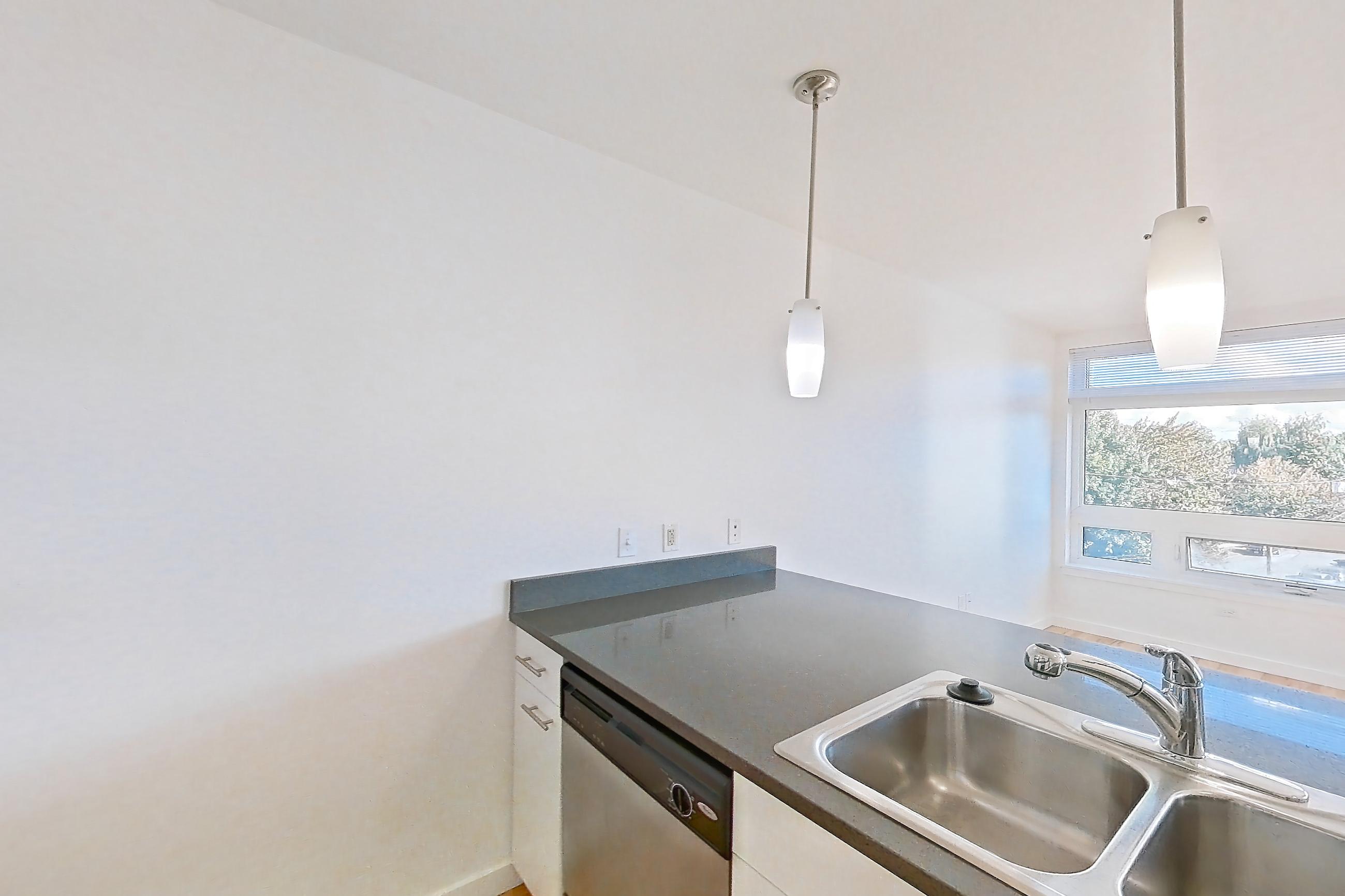Kitchen with dark countertops, dark stone countertops, dishwasher, electric range, light countertops, light wood-finish flooring, microwave, oven/range, refrigerator, and stainless steel appliances, Apartment 0421 at Circa Greenlake