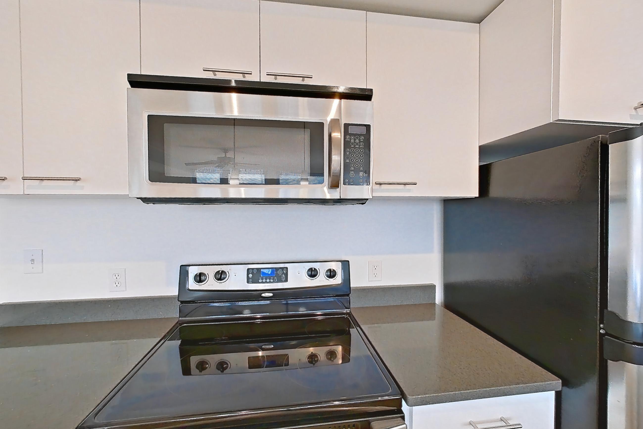 Kitchen with dark countertops, dark stone countertops, dishwasher, electric range, light countertops, light wood-finish flooring, microwave, oven/range, refrigerator, and stainless steel appliances, Apartment 0421 at Circa Greenlake