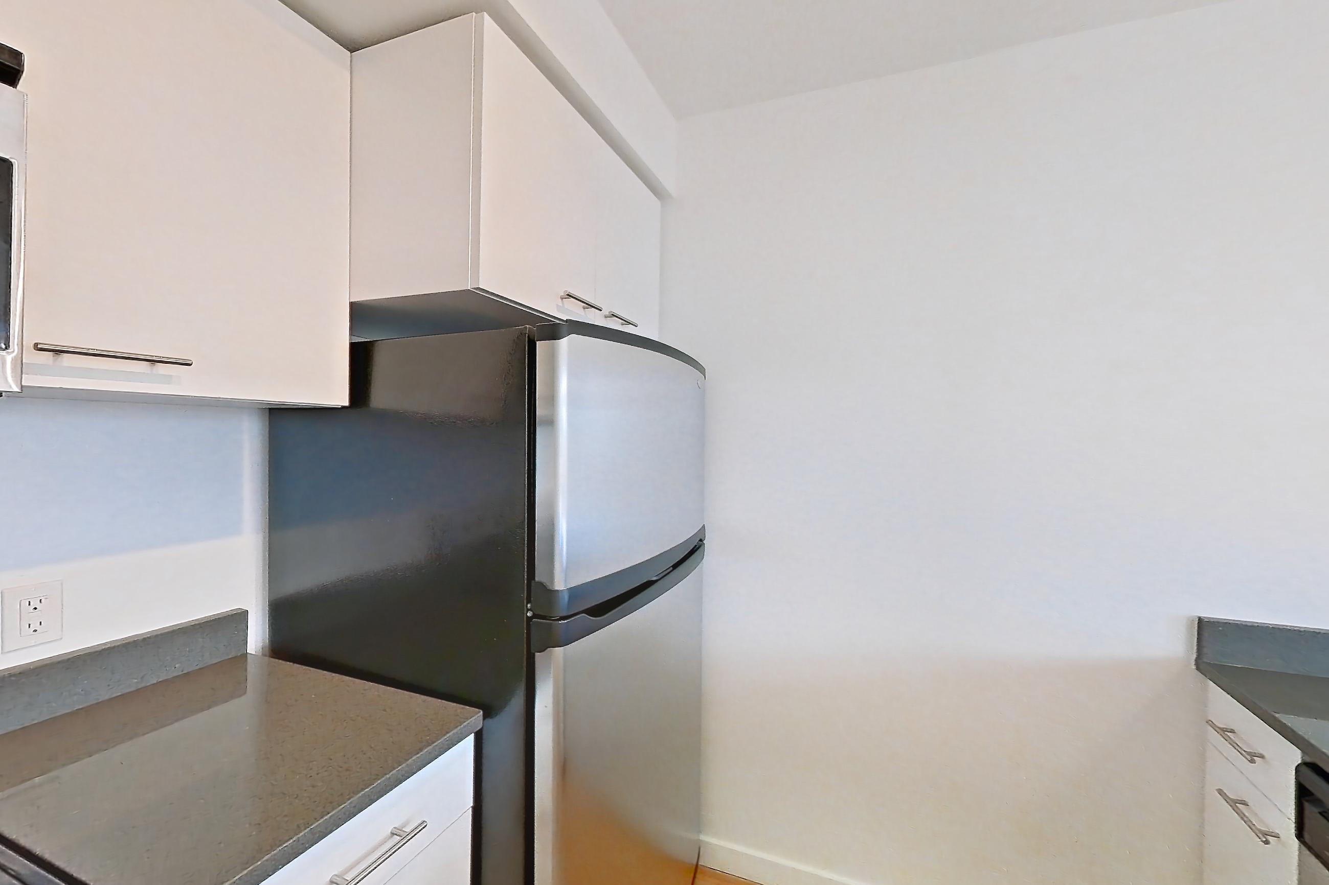 Kitchen with dark countertops, dark stone countertops, dishwasher, electric range, light countertops, light wood-finish flooring, microwave, oven/range, refrigerator, and stainless steel appliances, Apartment 0421 at Circa Greenlake