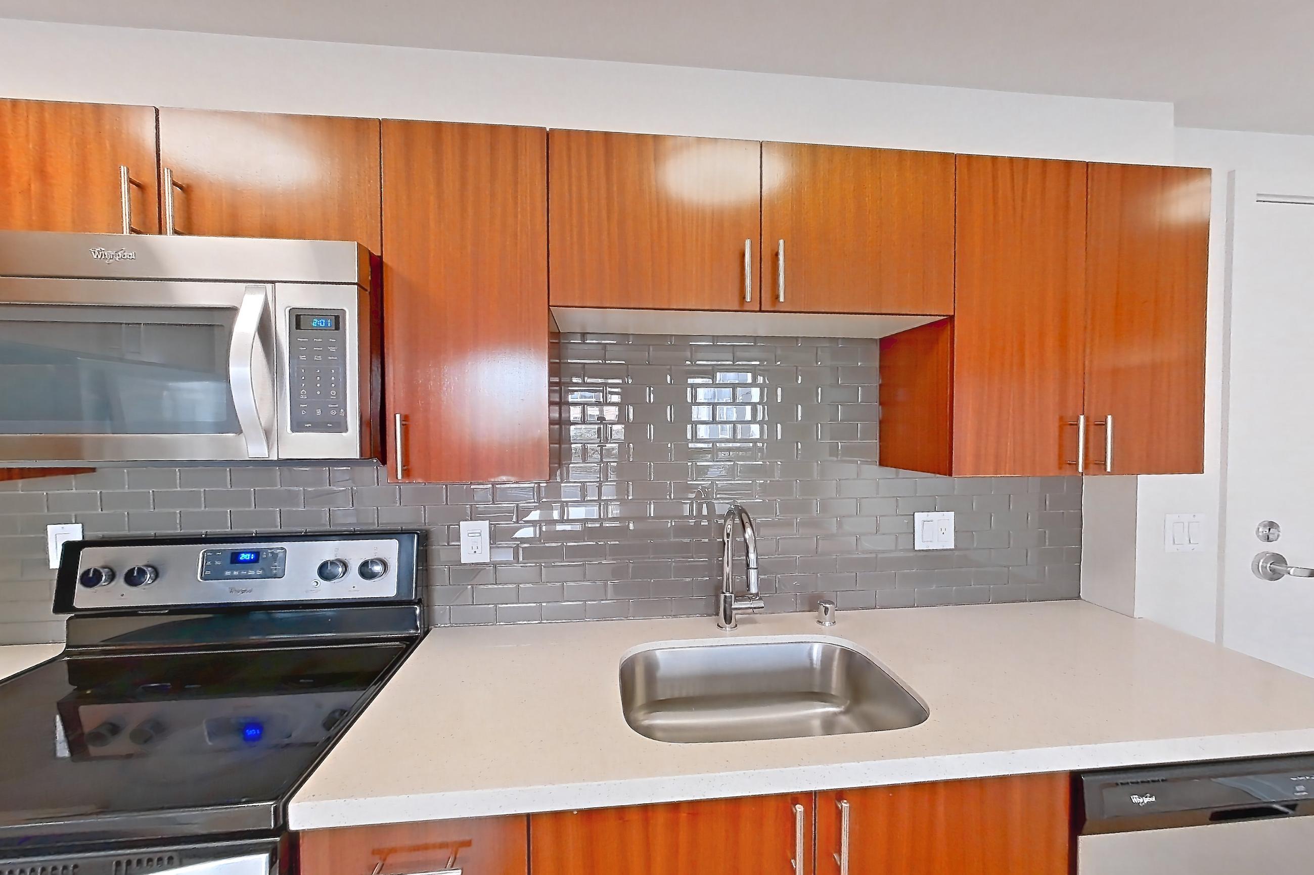 Kitchen with dishwasher, electric range, light countertops, light stone countertops, light wood-finish flooring, microwave, oven/range, refrigerator, and stainless steel appliances, Apartment L207 at Union SLU