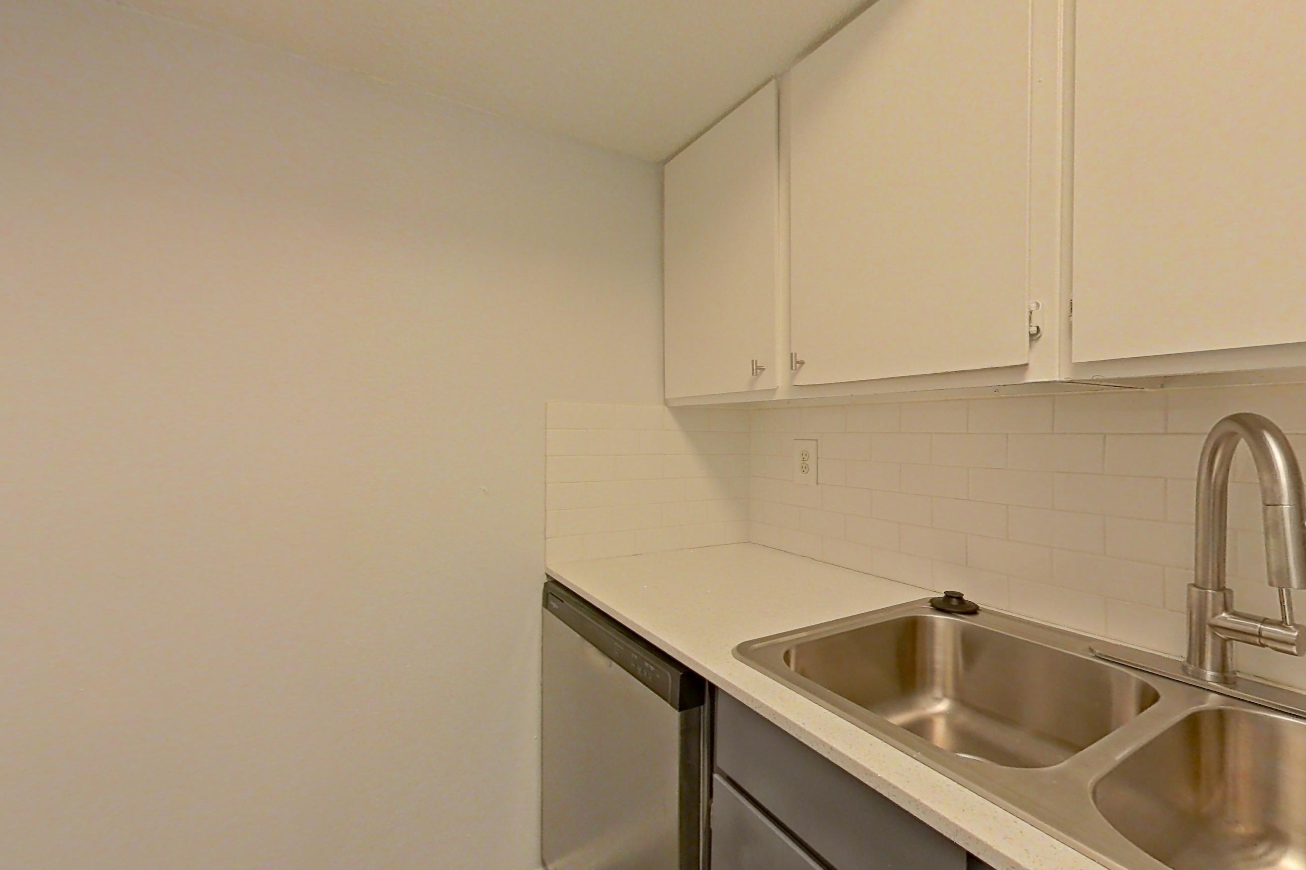 Kitchen with dark wood-finish flooring, dishwasher, electric range, light countertops, light stone countertops, oven/range, range hood, refrigerator, stainless steel appliances, and white appliances, Apartment 1904 at The Cove Apartments