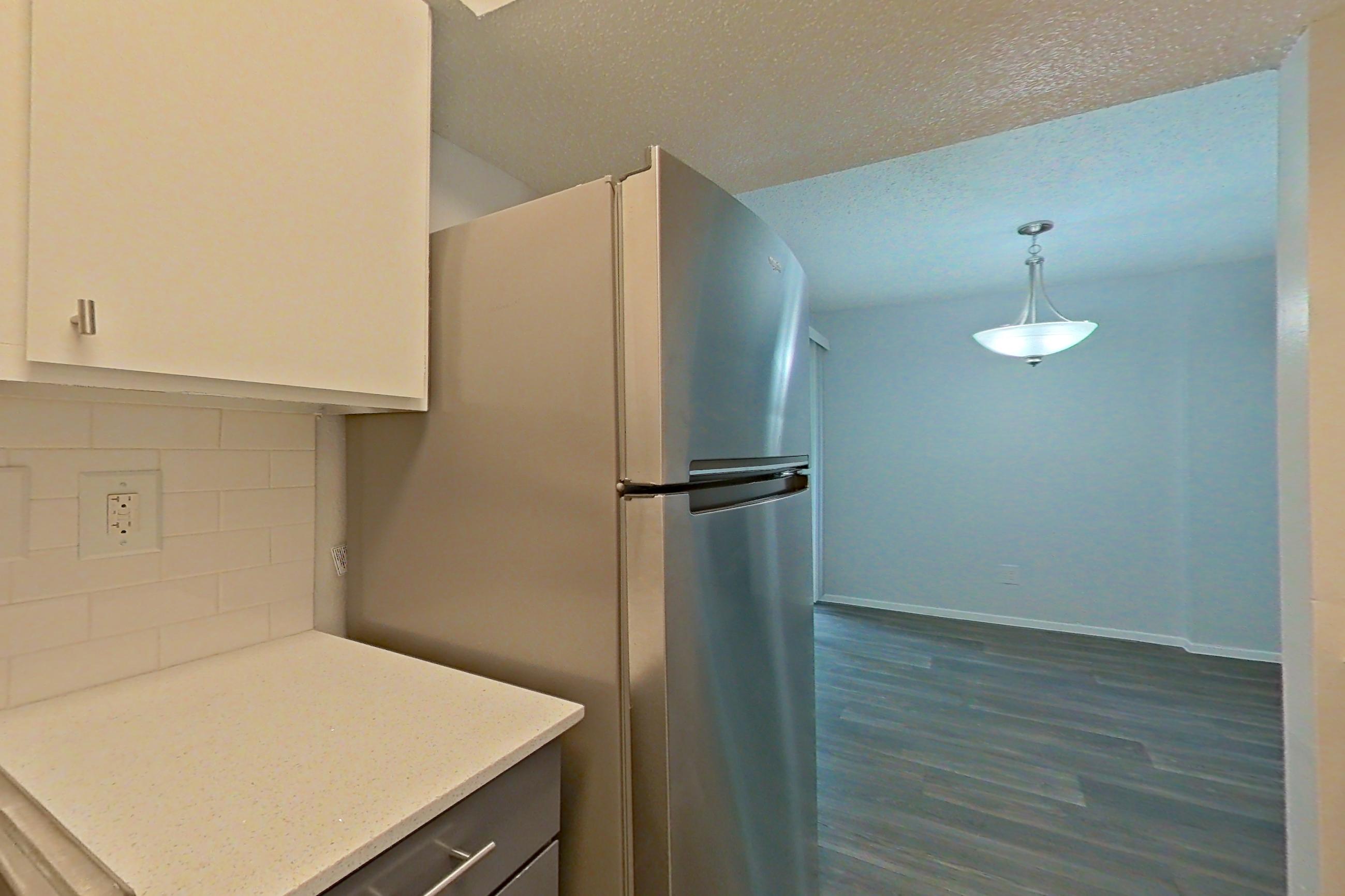 Kitchen with dark wood-finish flooring, dishwasher, electric range, light countertops, light stone countertops, oven/range, range hood, refrigerator, stainless steel appliances, and white appliances, Apartment 1904 at The Cove Apartments