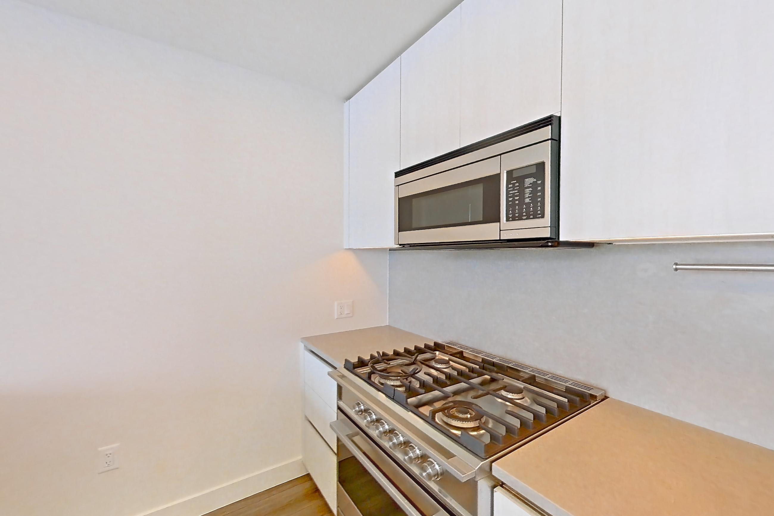 Kitchen with gas range, light countertops, light stone countertops, light wood-finish flooring, microwave, oven/range, and stainless steel appliances, Apartment 3213 at Alloy