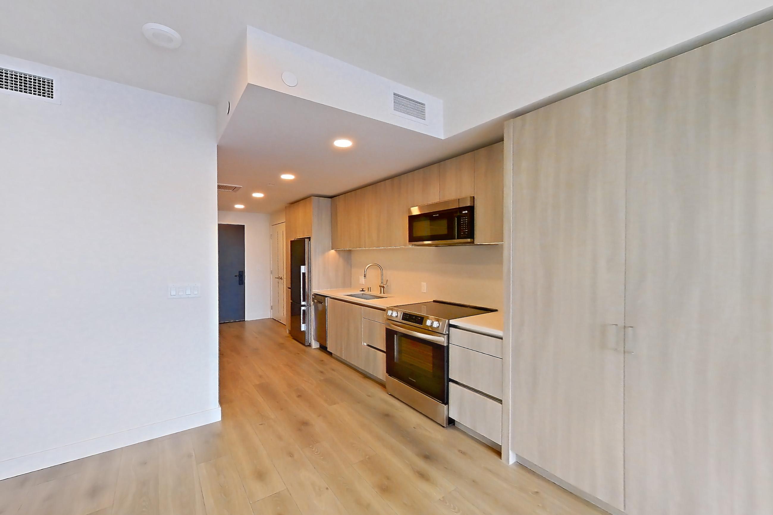 Living room with electric range, light countertops, light wood-finish flooring, microwave, oven/range, and stainless steel appliances, Apartment 1715 at Alloy