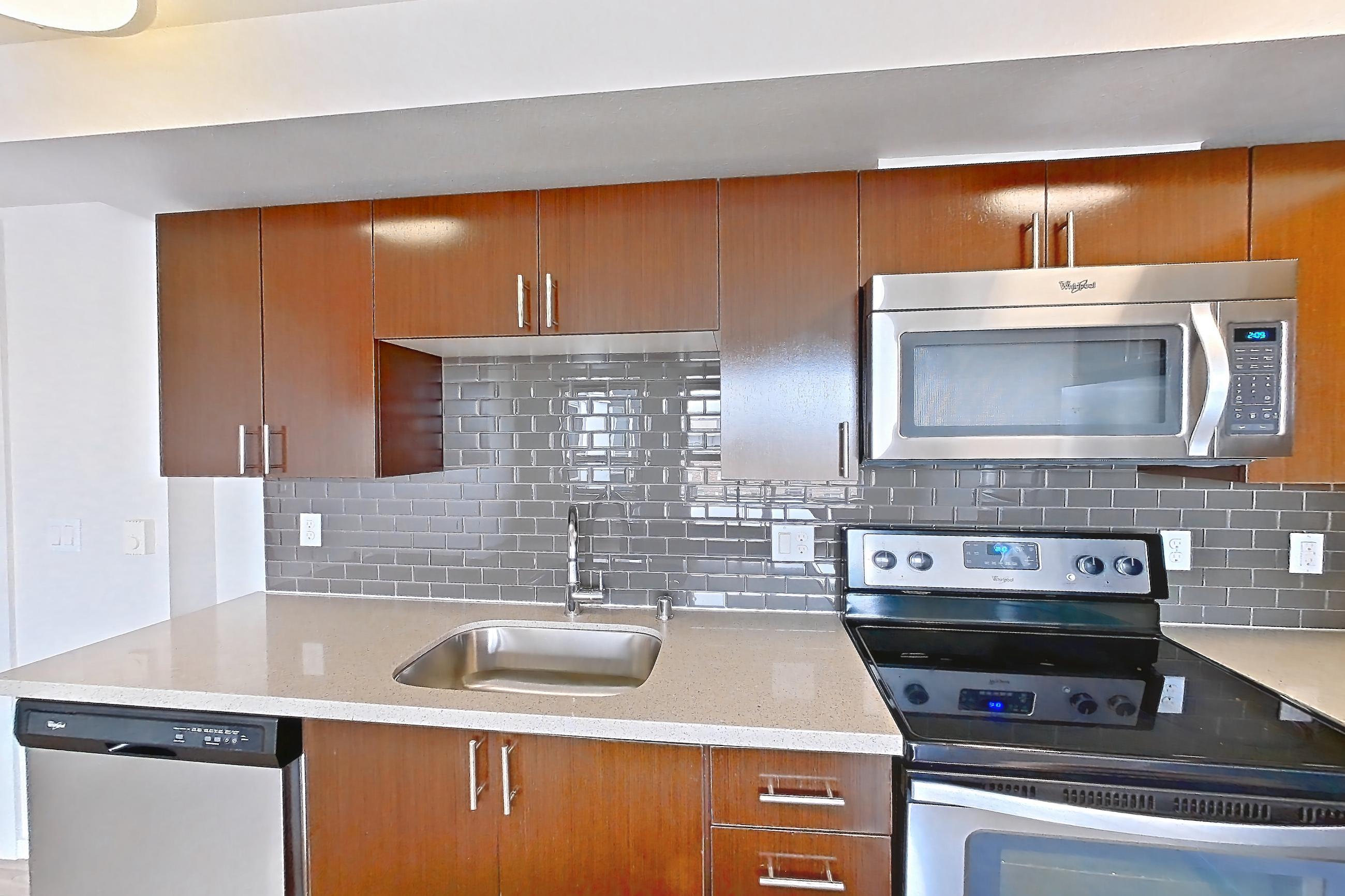 Kitchen with dishwasher, electric range, light countertops, light stone countertops, light wood-finish flooring, microwave, oven/range, refrigerator, and stainless steel appliances, Apartment L635 at Union SLU
