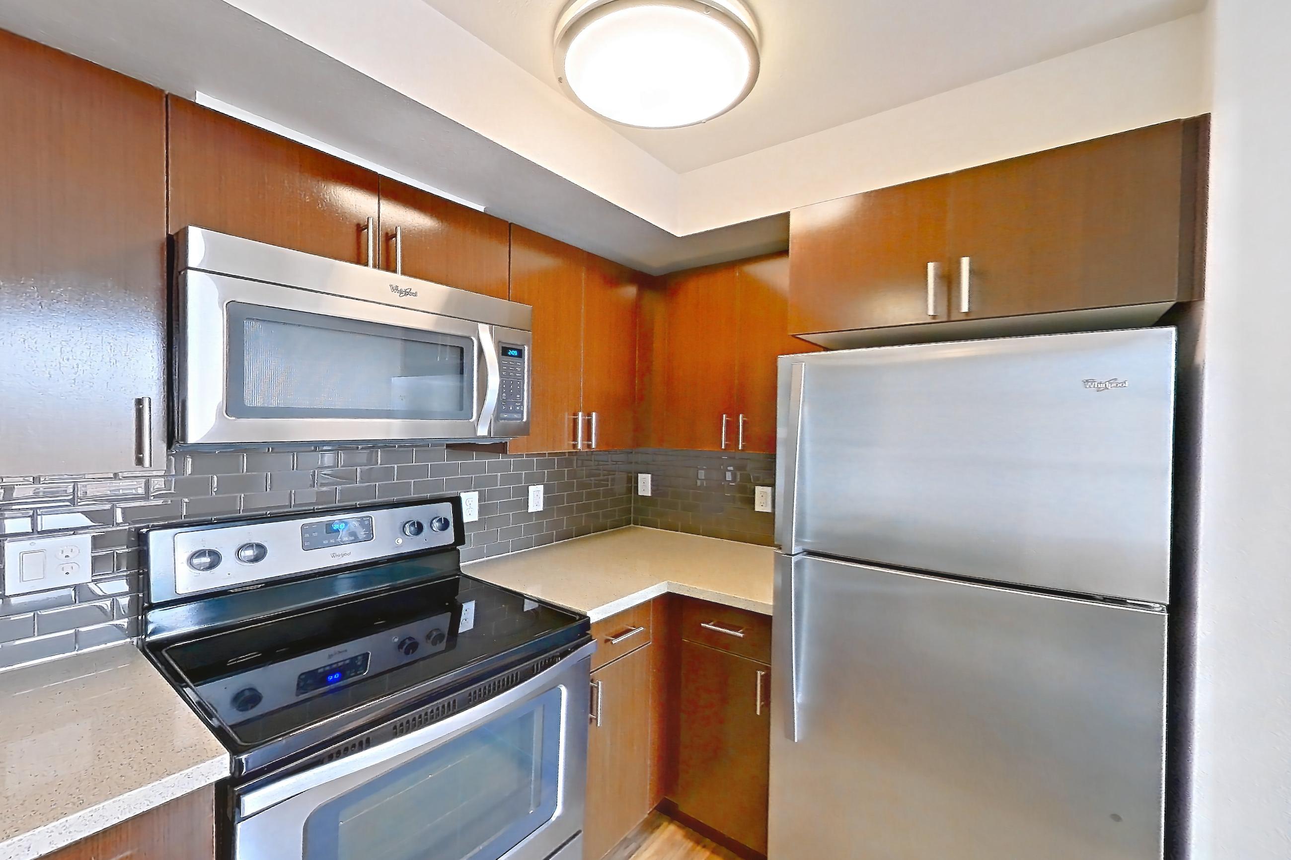 Kitchen with dishwasher, electric range, light countertops, light stone countertops, light wood-finish flooring, microwave, oven/range, refrigerator, and stainless steel appliances, Apartment L635 at Union SLU