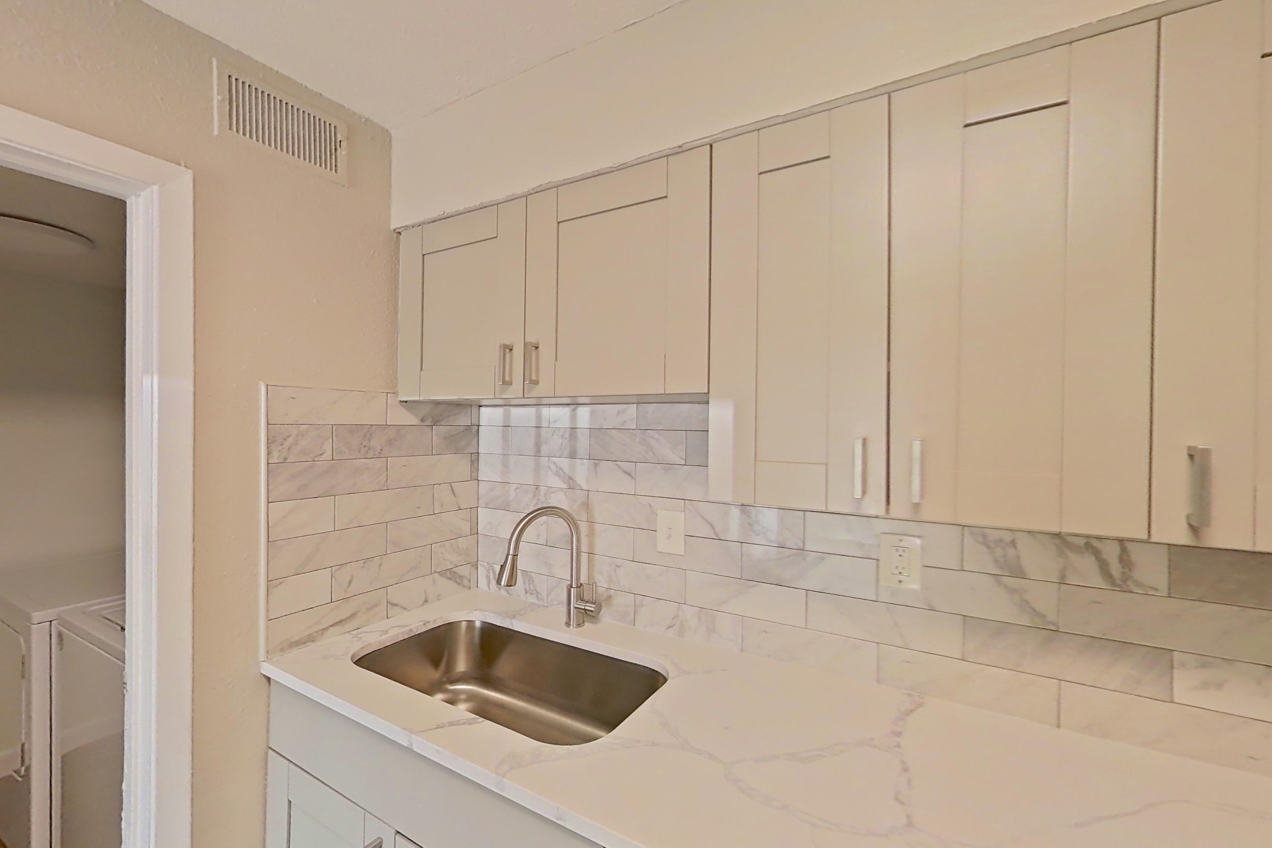 Kitchen with black appliances, dishwasher, electric range, light countertops, light stone countertops, light wood-finish flooring, microwave, oven/range, refrigerator, and stainless steel appliances, Apartment 0303 at Dunwoody Glen