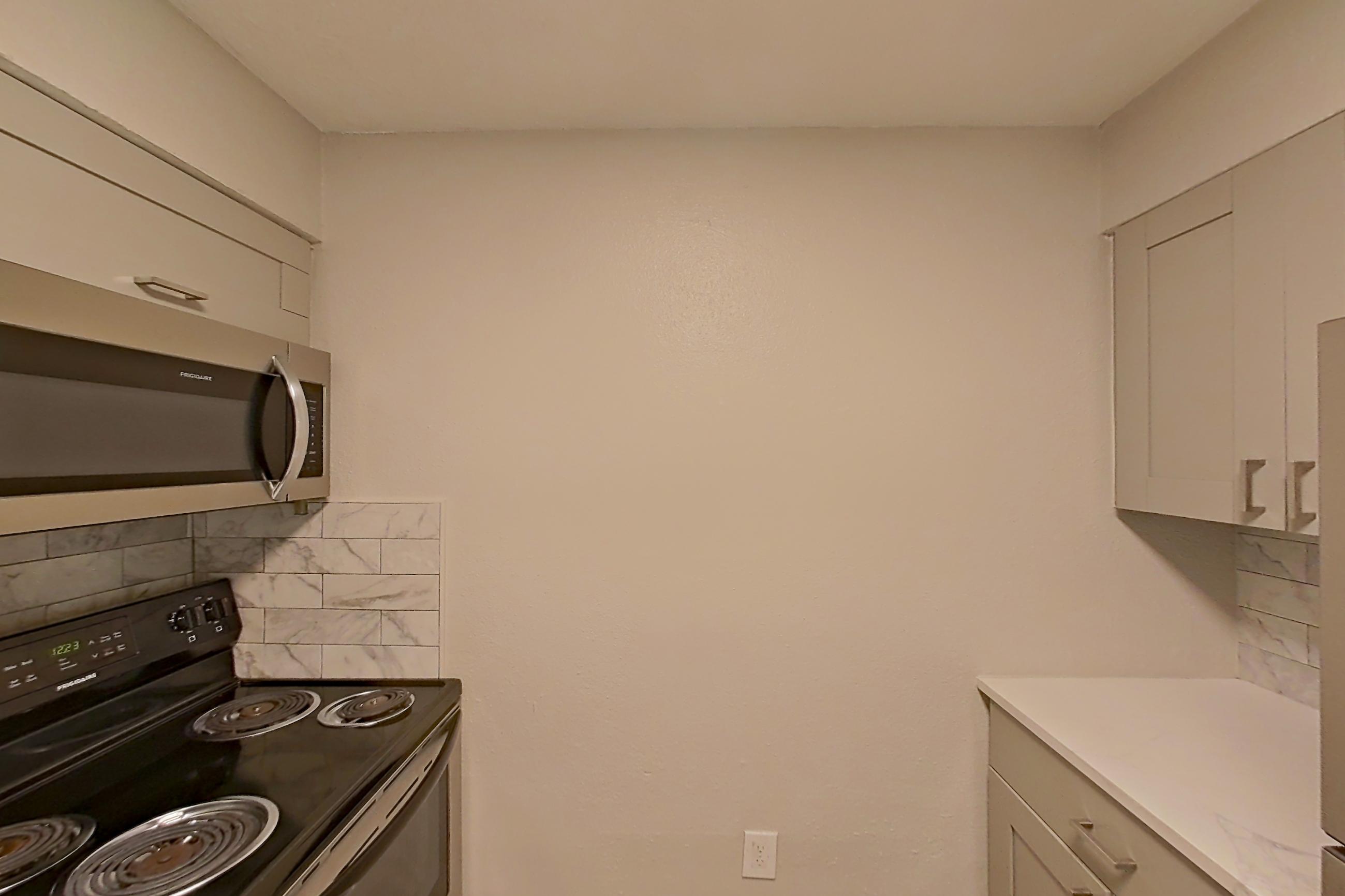 Kitchen with black appliances, dishwasher, electric range, light countertops, light stone countertops, light wood-finish flooring, microwave, oven/range, refrigerator, and stainless steel appliances, Apartment 0303 at Dunwoody Glen