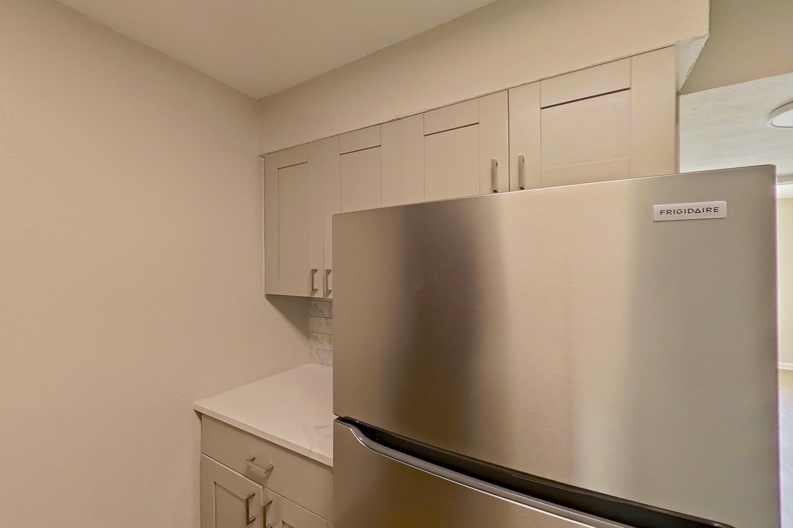 Kitchen with black appliances, dishwasher, electric range, light countertops, light stone countertops, light wood-finish flooring, microwave, oven/range, refrigerator, and stainless steel appliances, Apartment 0303 at Dunwoody Glen