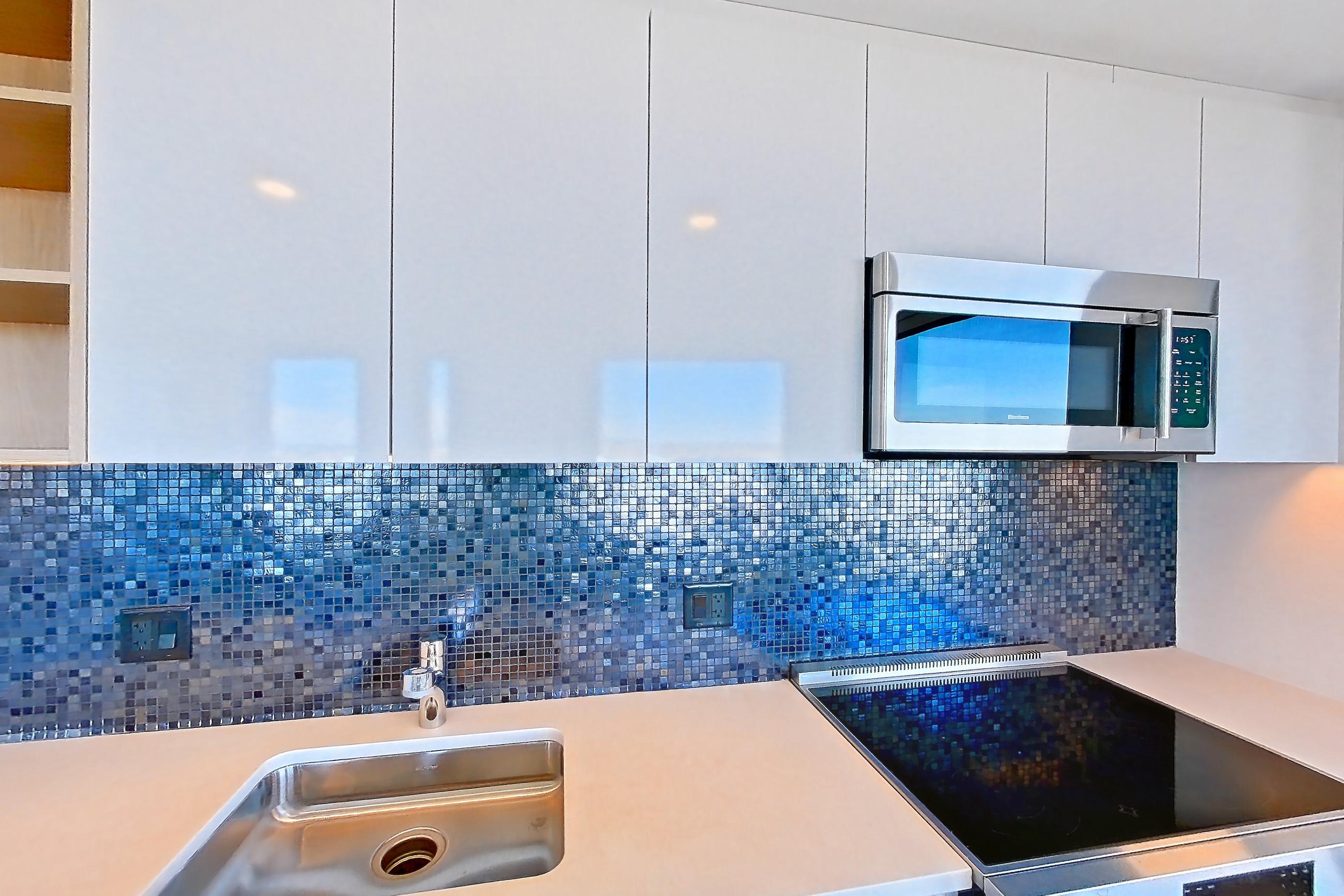 Kitchen with dishwasher, electric range, light countertops, light wood-finish flooring, microwave, oven/range, refrigerator, and stainless steel appliances, Apartment 2802 at The Sudbury