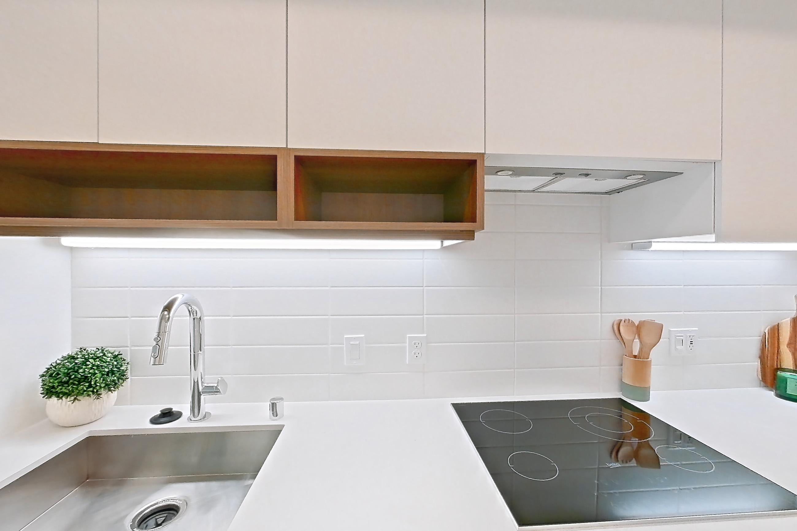Kitchen with black appliances, cooktop, electric cooktop, light wood-finish flooring, oven/range, and stainless steel appliances, Apartment 205 at Akin Residences