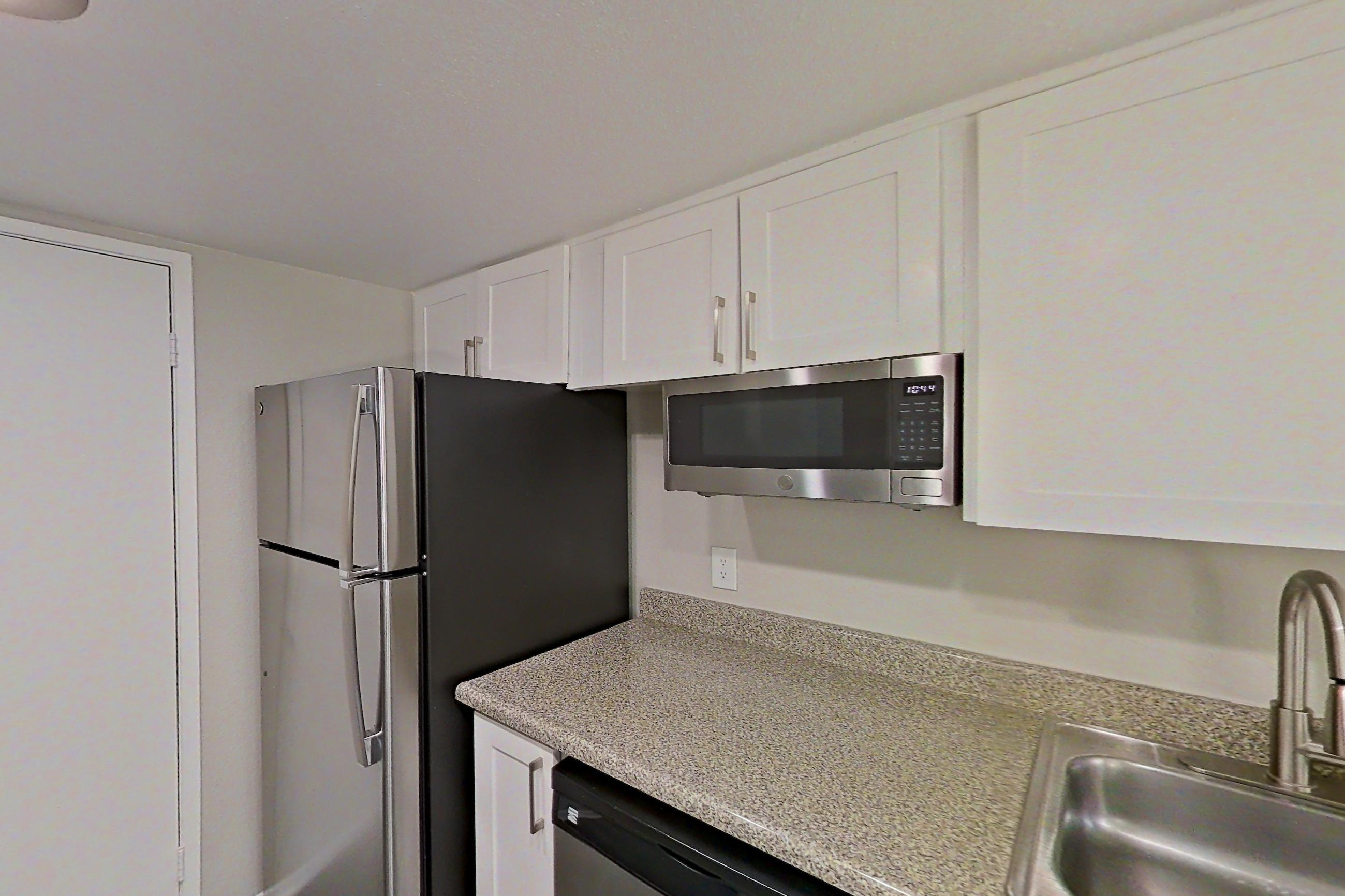Kitchen with dishwasher, electric range, light countertops, light stone countertops, light wood-finish flooring, microwave, oven/range, refrigerator, and stainless steel appliances, Apartment 07 at Avana Rancho Cucamonga