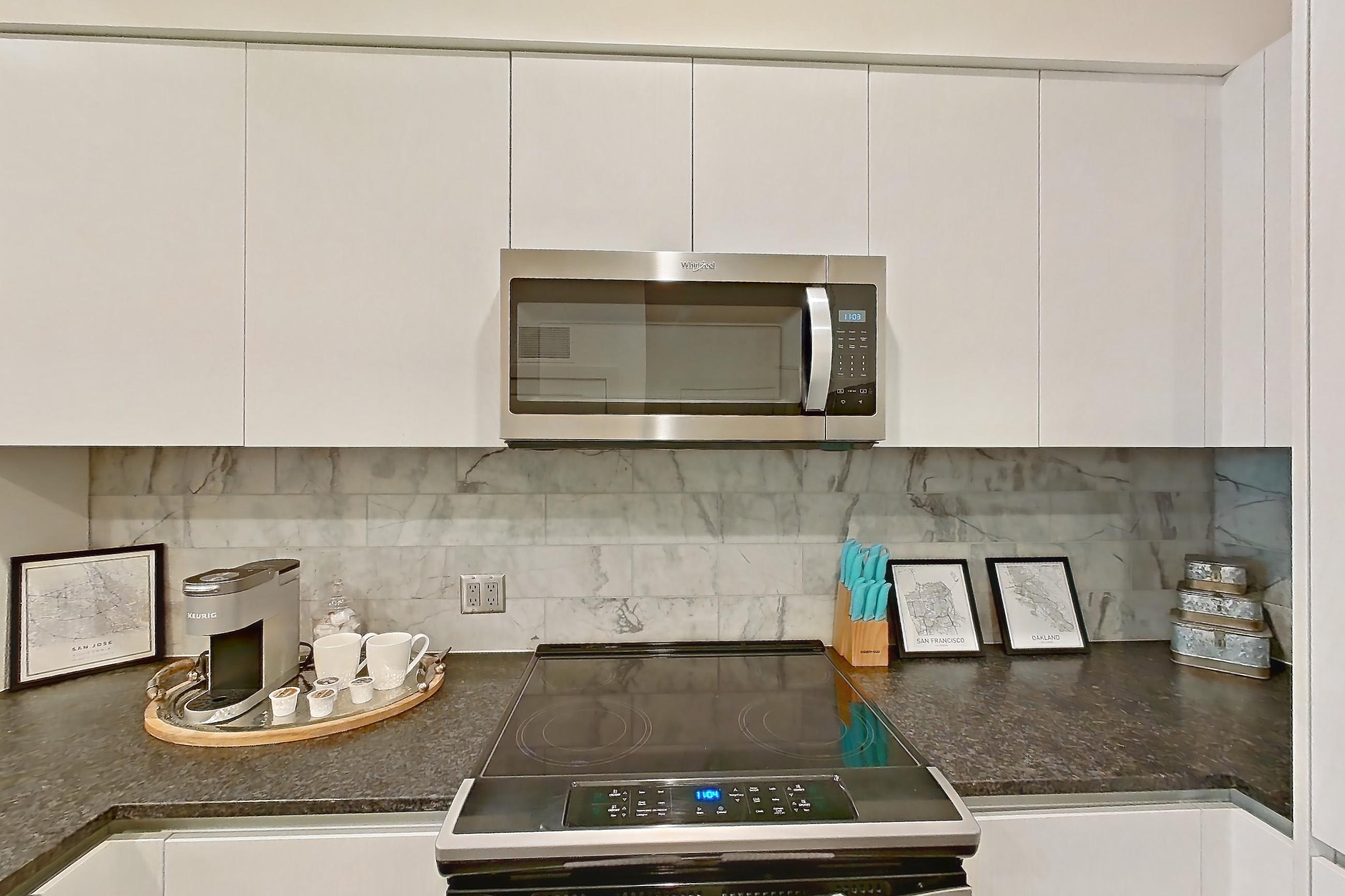 Kitchen with dark countertops, dark stone countertops, dark wood-finish flooring, dishwasher, electric range, light countertops, microwave, oven/range, refrigerator, stainless steel appliances, and water & ice dispenser, Apartment 220 at Diridon West