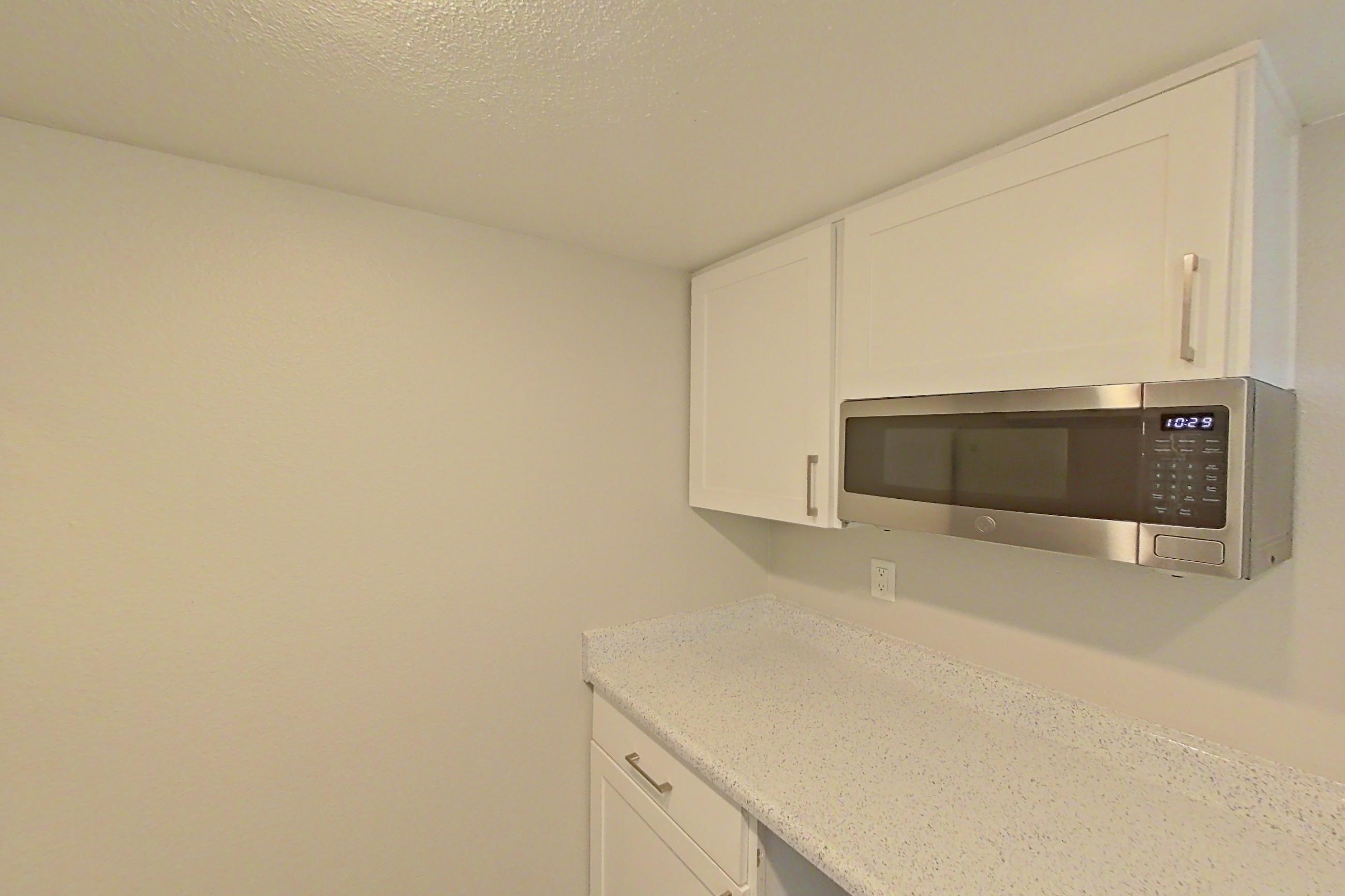 Kitchen with electric range, light stone countertops, light wood-finish flooring, microwave, oven/range, refrigerator, and stainless steel appliances, Apartment 24 at Avana Rancho Cucamonga