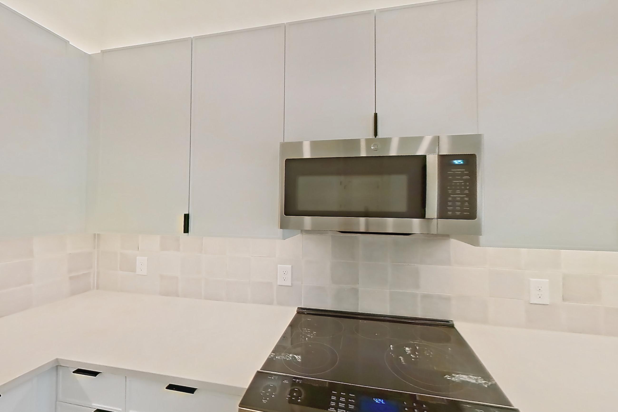 Kitchen with dishwasher, electric range, light countertops, light wood-finish flooring, microwave, oven/range, range hood, refrigerator, and stainless steel appliances, Apartment 121 at Lantower Midtown