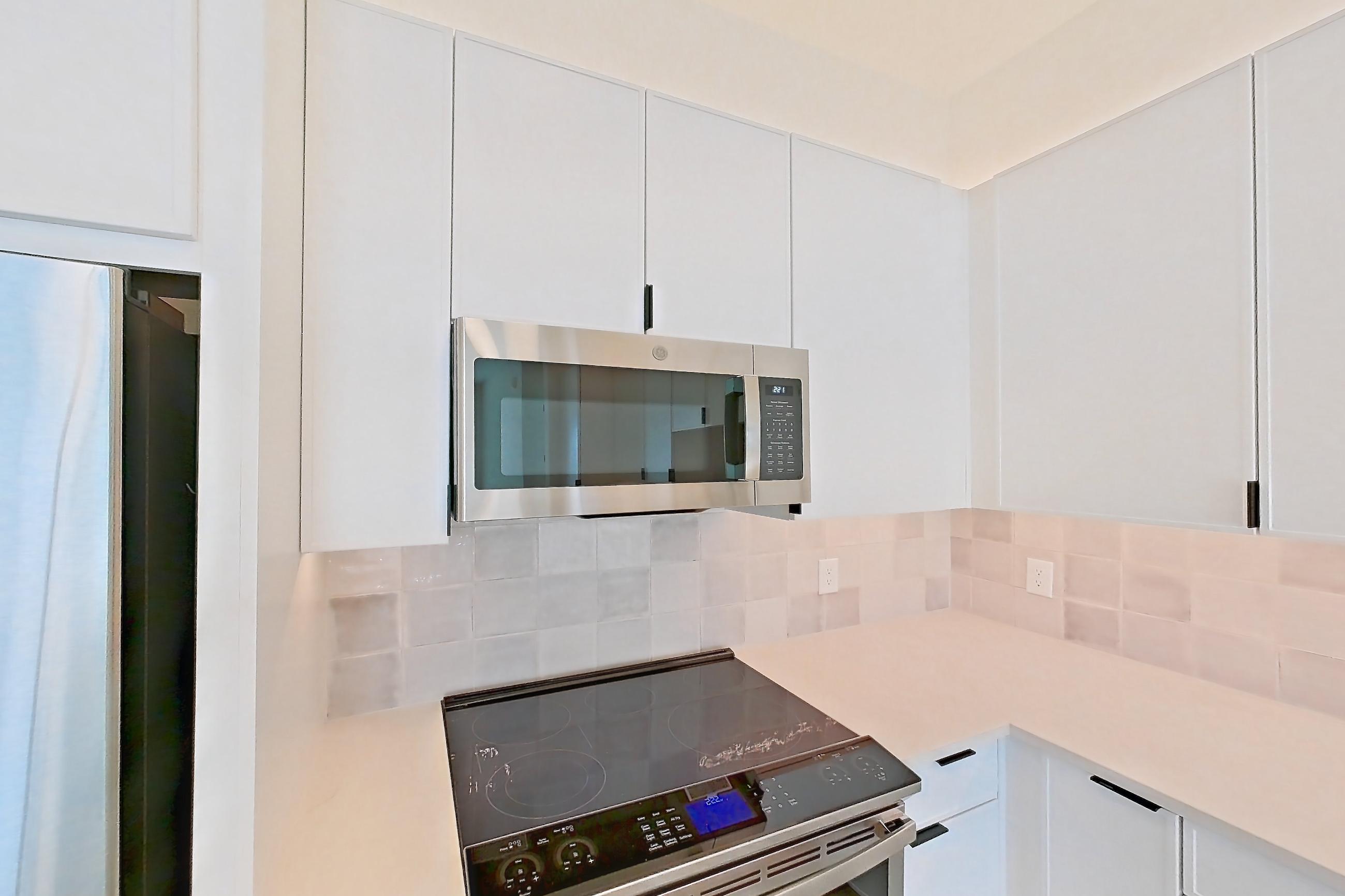 Kitchen with dishwasher, electric range, light countertops, light stone countertops, light wood-finish flooring, microwave, oven/range, refrigerator, and stainless steel appliances, Apartment 266 at Lantower Midtown