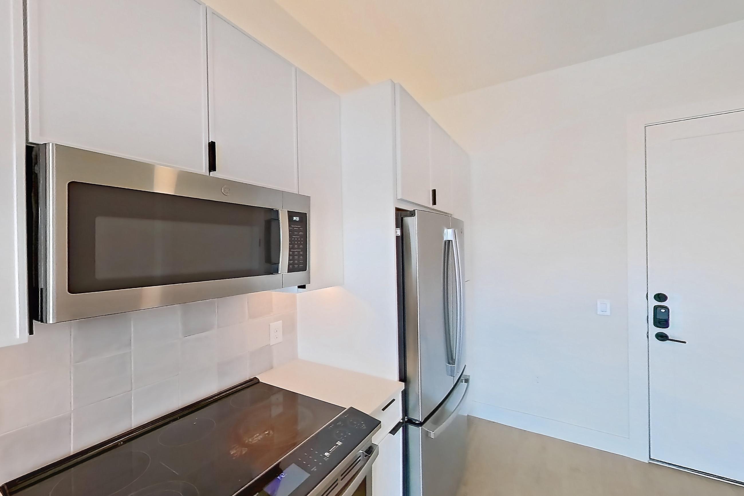Kitchen with dishwasher, electric range, light countertops, light stone countertops, light wood-finish flooring, microwave, oven/range, refrigerator, stainless steel appliances, and wood-finish flooring, Apartment 314 at Lantower Midtown