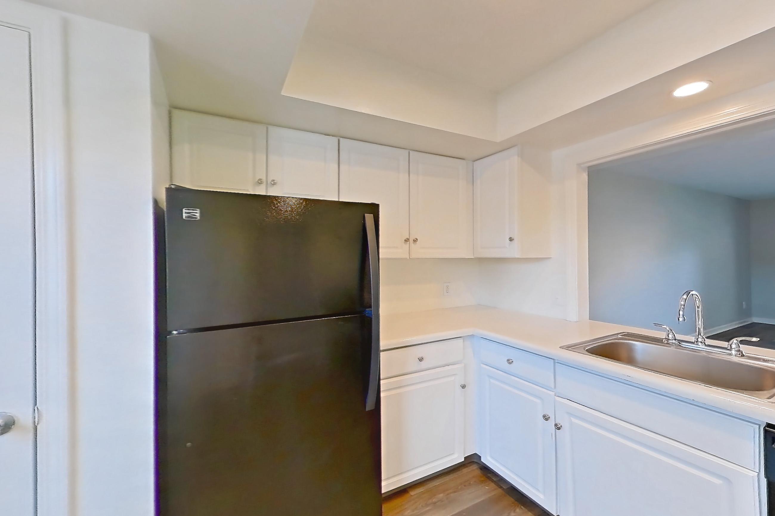 Kitchen with black appliances, electric range, light countertops, light wood-finish flooring, oven/range, range hood, refrigerator, and stainless steel appliances, Apartment 2627 at Canterbury Green