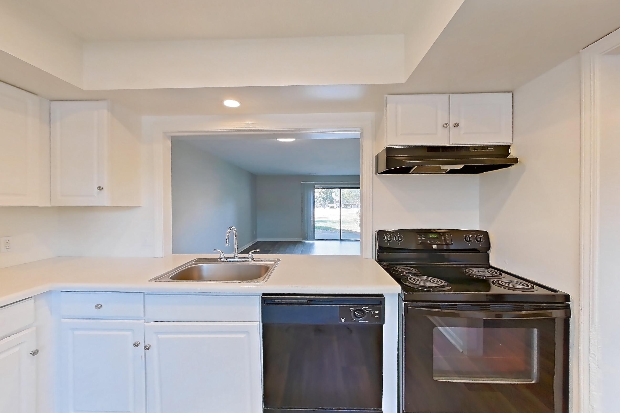 Kitchen with black appliances, electric range, light countertops, light wood-finish flooring, oven/range, range hood, refrigerator, and stainless steel appliances, Apartment 2627 at Canterbury Green