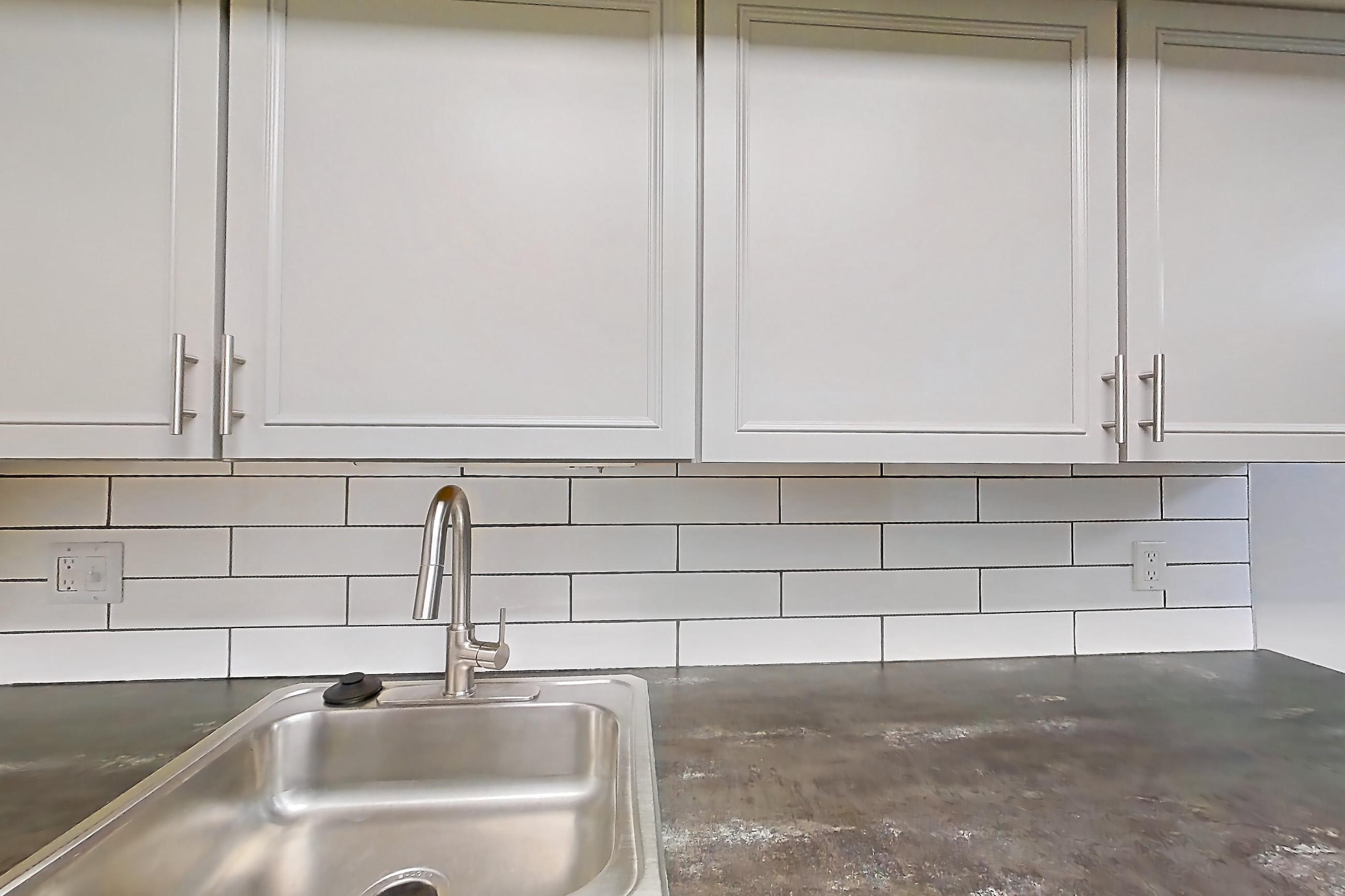 Kitchen with black appliances, dark countertops, electric range, in-unit laundry, light wood-finish flooring, oven/range, range hood, refrigerator, and stainless steel appliances, Apartment 2815-1 at Canterbury Green