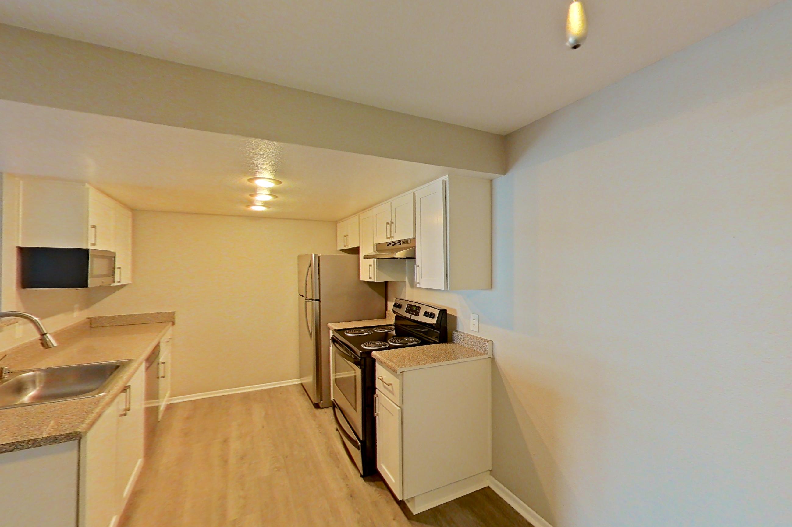 Dining area with electric range, light countertops, light wood-finish flooring, microwave, oven/range, stainless steel appliances, and white appliances, Apartment 07 at Avana Rancho Cucamonga