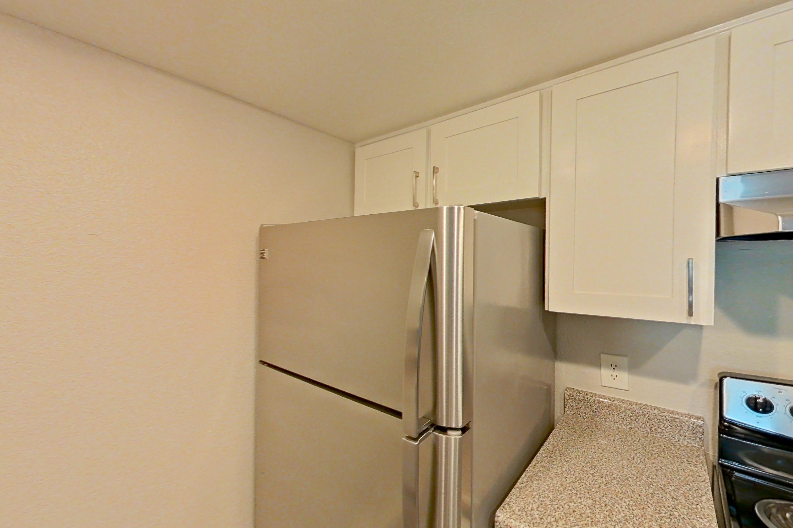 Kitchen with dishwasher, electric range, light countertops, light stone countertops, light wood-finish flooring, oven/range, range hood, refrigerator, and stainless steel appliances, Apartment 07 at Avana Rancho Cucamonga