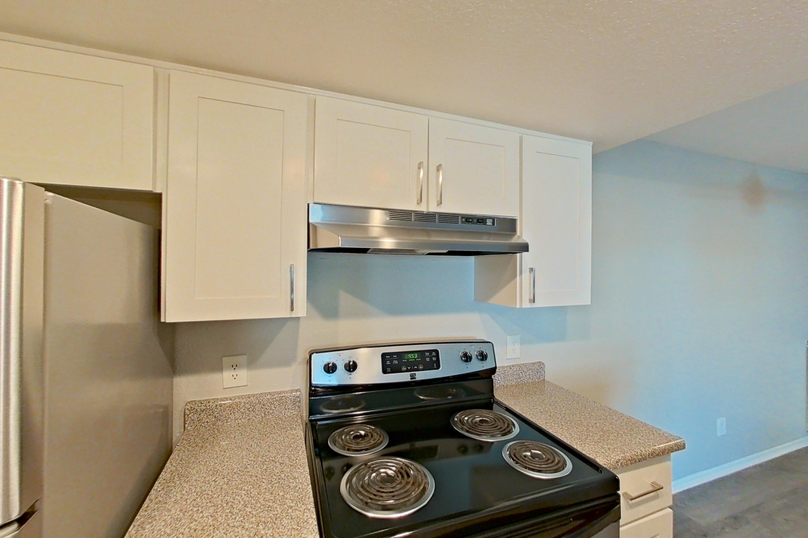 Kitchen with dishwasher, electric range, light countertops, light stone countertops, light wood-finish flooring, oven/range, range hood, refrigerator, and stainless steel appliances, Apartment 07 at Avana Rancho Cucamonga