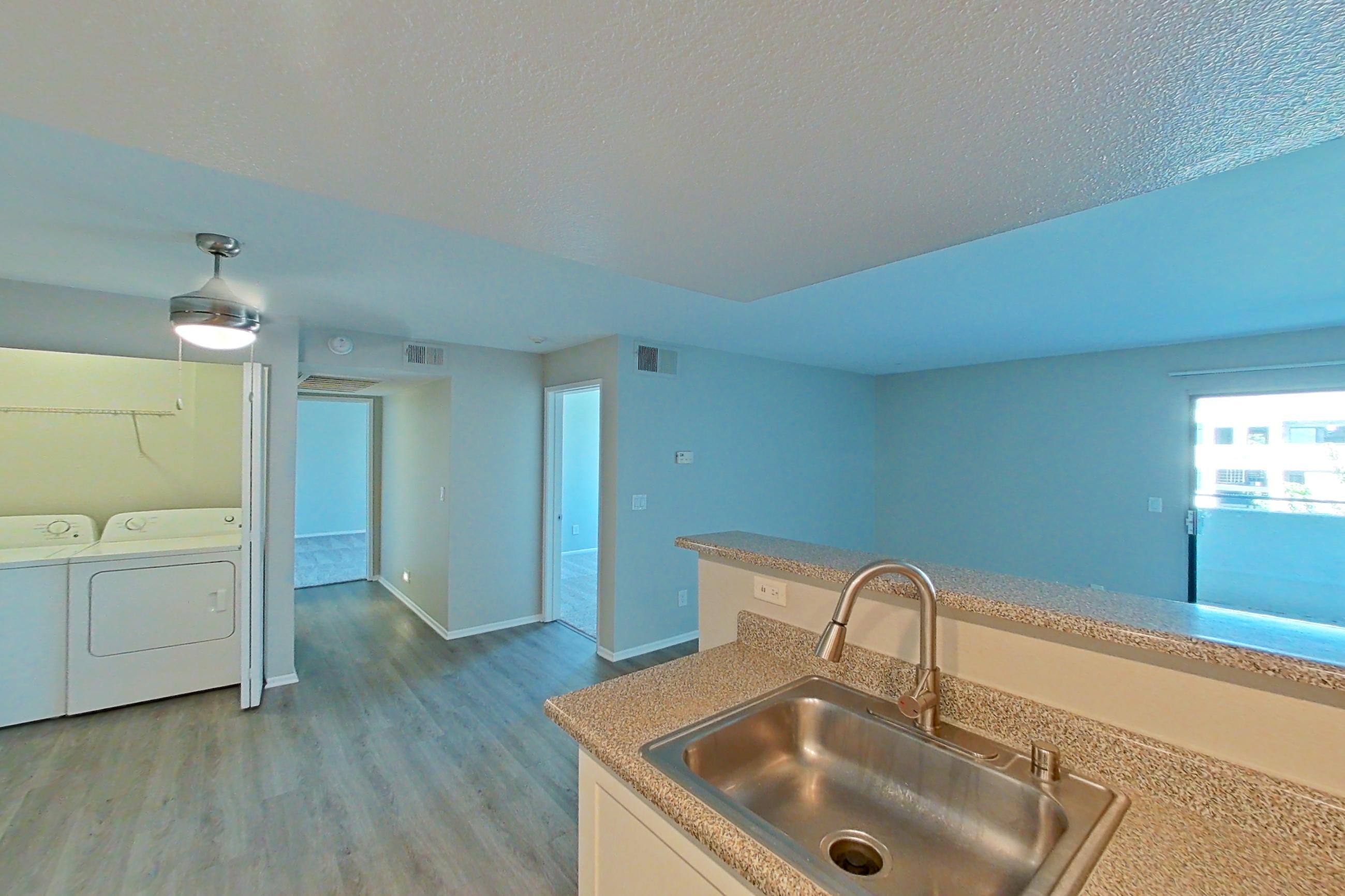 Kitchen with dishwasher, electric range, in-unit laundry, light countertops, light stone countertops, light wood-finish flooring, microwave, oven/range, range hood, and stainless steel appliances, Apartment 11 at Avana Rancho Cucamonga