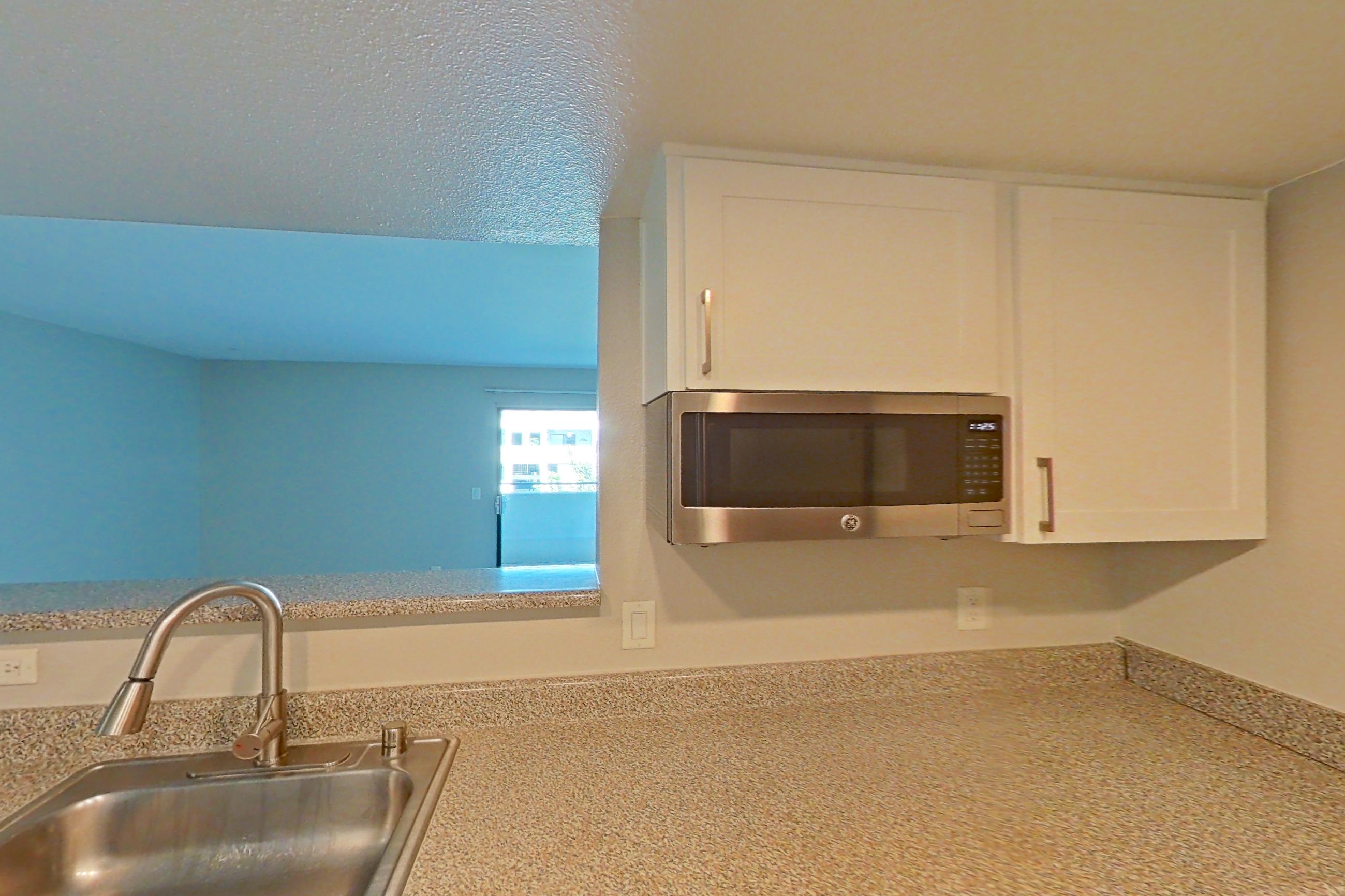 Kitchen with dishwasher, electric range, in-unit laundry, light countertops, light stone countertops, light wood-finish flooring, microwave, oven/range, range hood, and stainless steel appliances, Apartment 11 at Avana Rancho Cucamonga