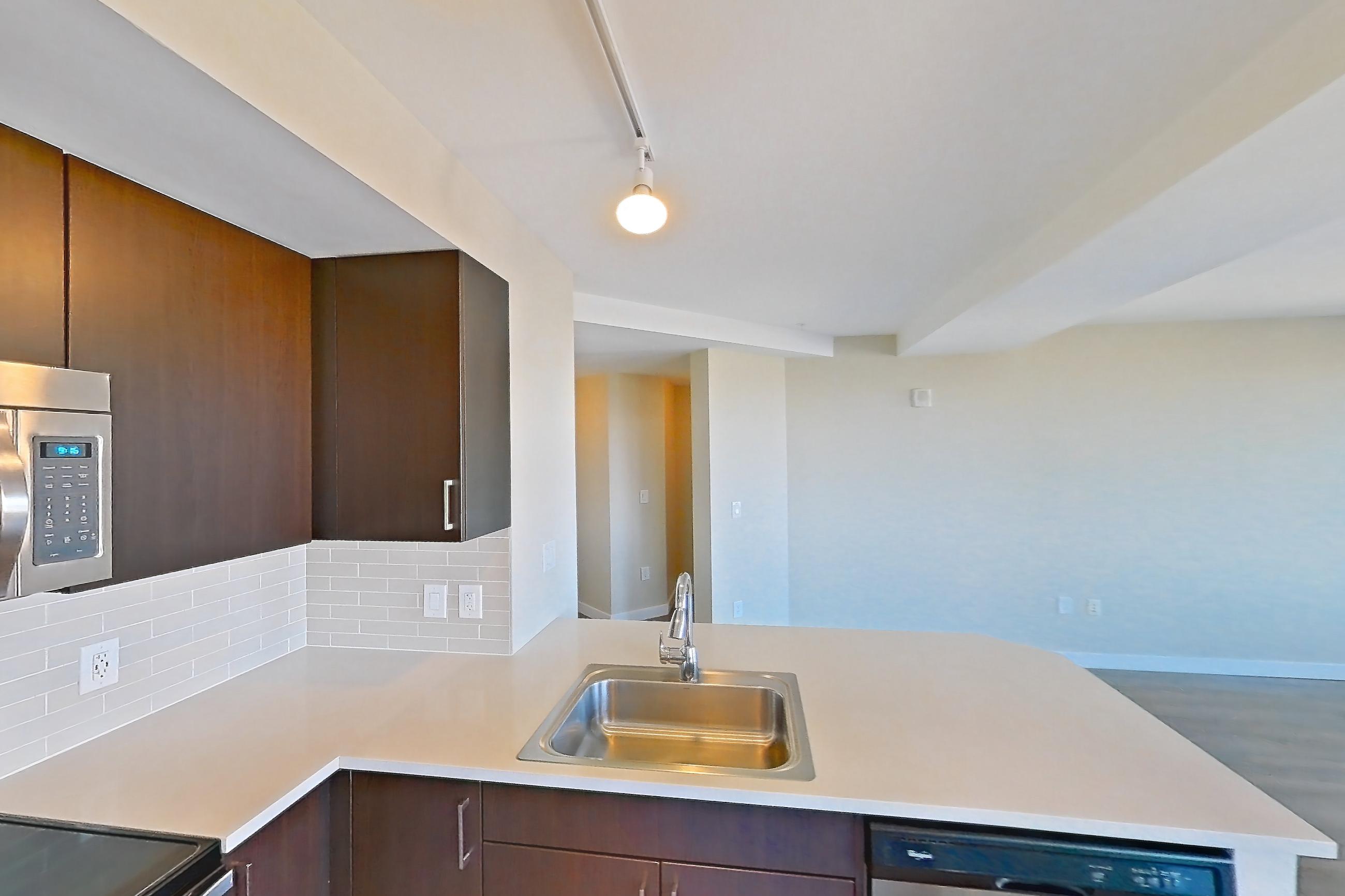Kitchen with dishwasher, light countertops, light stone countertops, light wood-finish flooring, refrigerator, and stainless steel appliances, Apartment 2101 at Luka