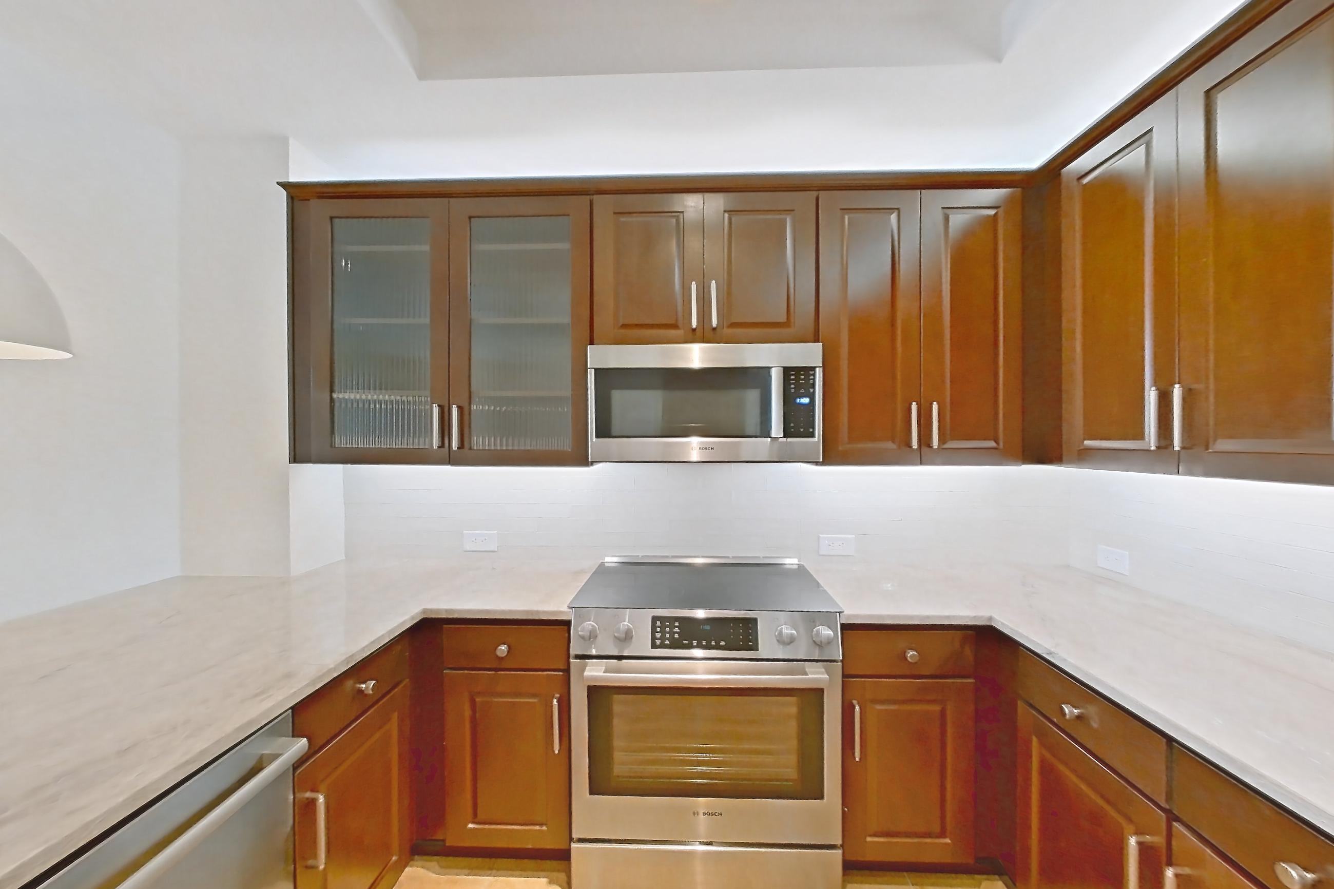 Kitchen with dishwasher, electric range, kitchen island, light countertops, light stone countertops, microwave, oven/range, refrigerator, stainless steel appliances, and water & ice dispenser, Apartment 2008 at Cortland on McKinney