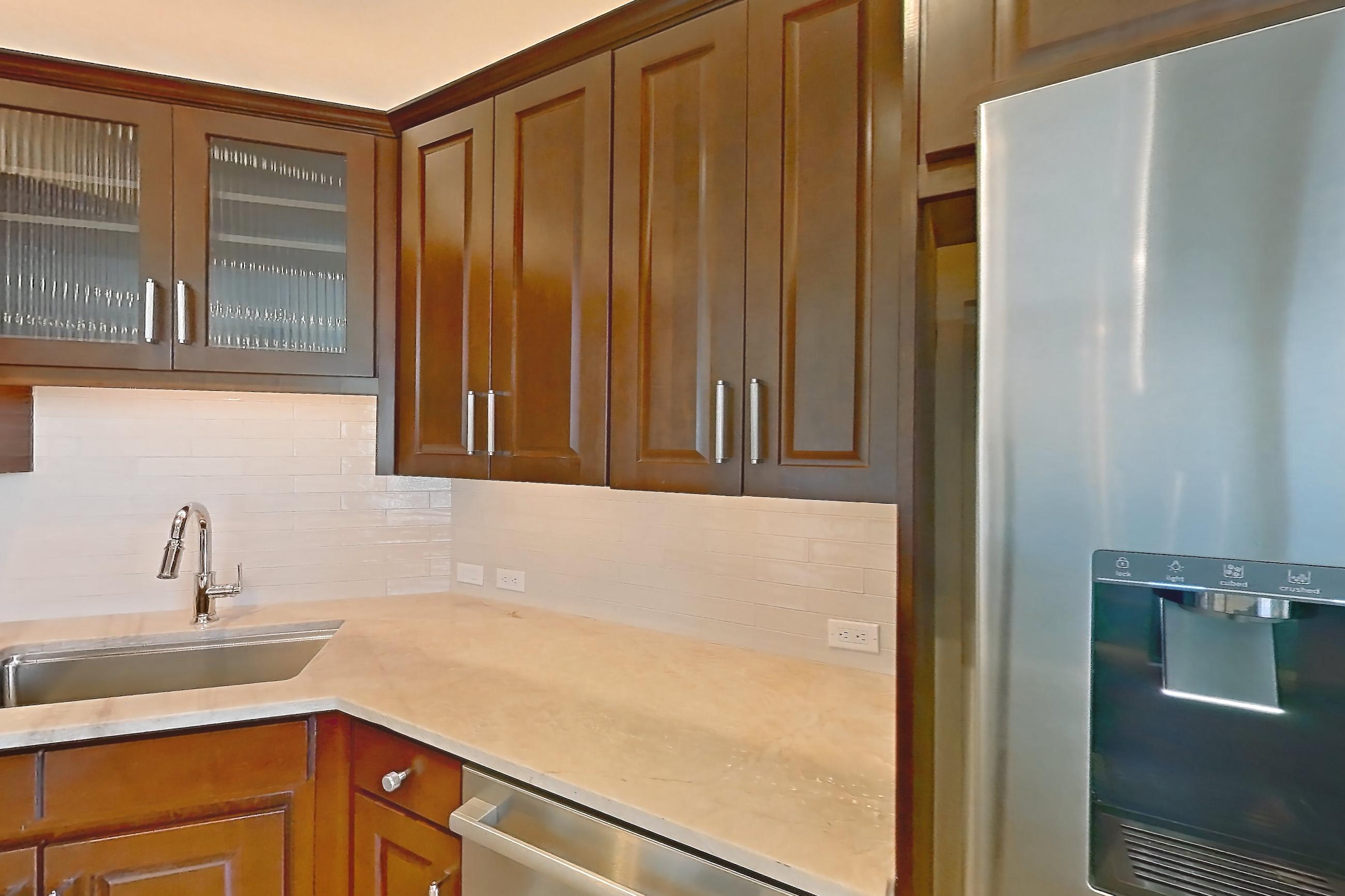 Kitchen with black appliances, built-in microwave, cooktop, dishwasher, double oven, electric cooktop, kitchen island, light countertops, light stone countertops, light tile flooring, light wood-finish flooring, range hood, refrigerator, stainless steel appliances, and water & ice dispenser, Apartment 1507 at Cortland on McKinney