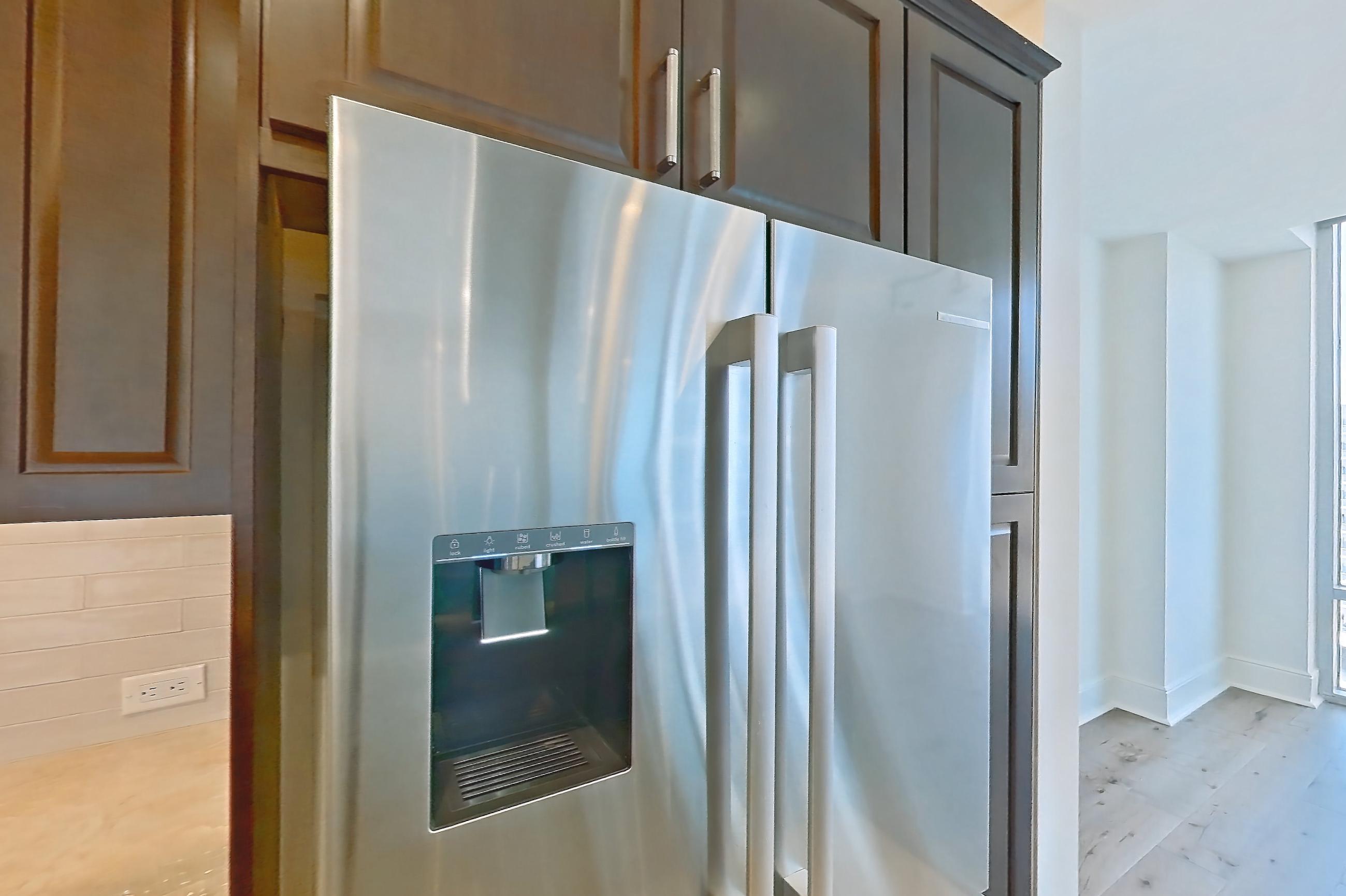 Kitchen with black appliances, built-in microwave, cooktop, dishwasher, double oven, electric cooktop, kitchen island, light countertops, light stone countertops, light tile flooring, light wood-finish flooring, range hood, refrigerator, stainless steel appliances, and water & ice dispenser, Apartment 1507 at Cortland on McKinney
