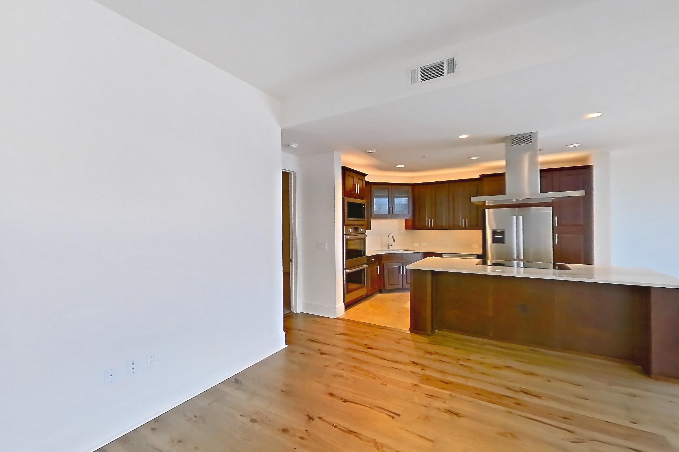 Living room with black appliances, city view, cooktop, double oven, electric cooktop, kitchen island, light stone countertops, light wood-finish flooring, range hood, refrigerator, and stainless steel appliances, Apartment 1507 at Cortland on McKinney
