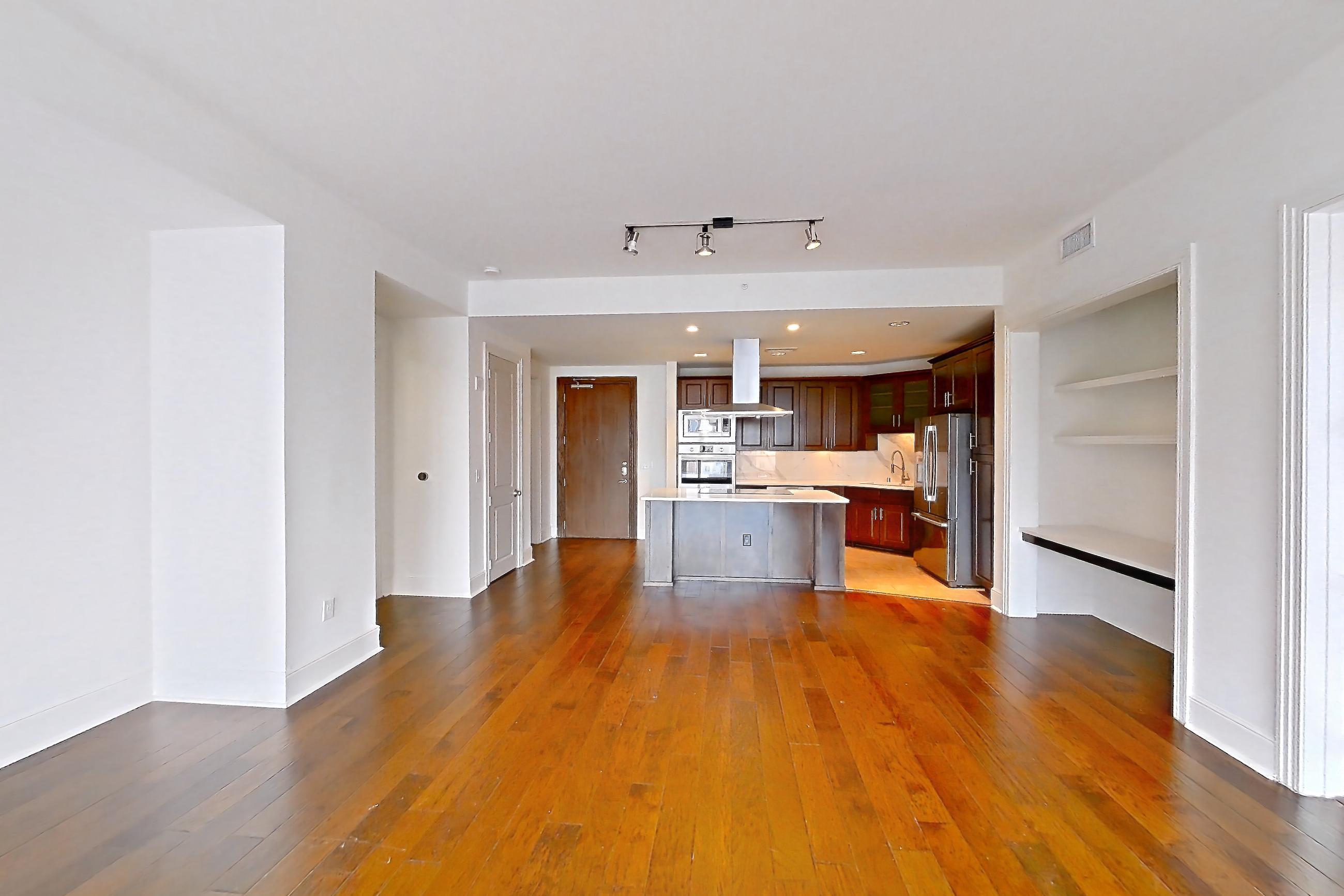 Living room with dark wood-finish flooring, kitchen island, light stone countertops, oven/range, range hood, refrigerator, and stainless steel appliances, Apartment 1709 at Cortland on McKinney