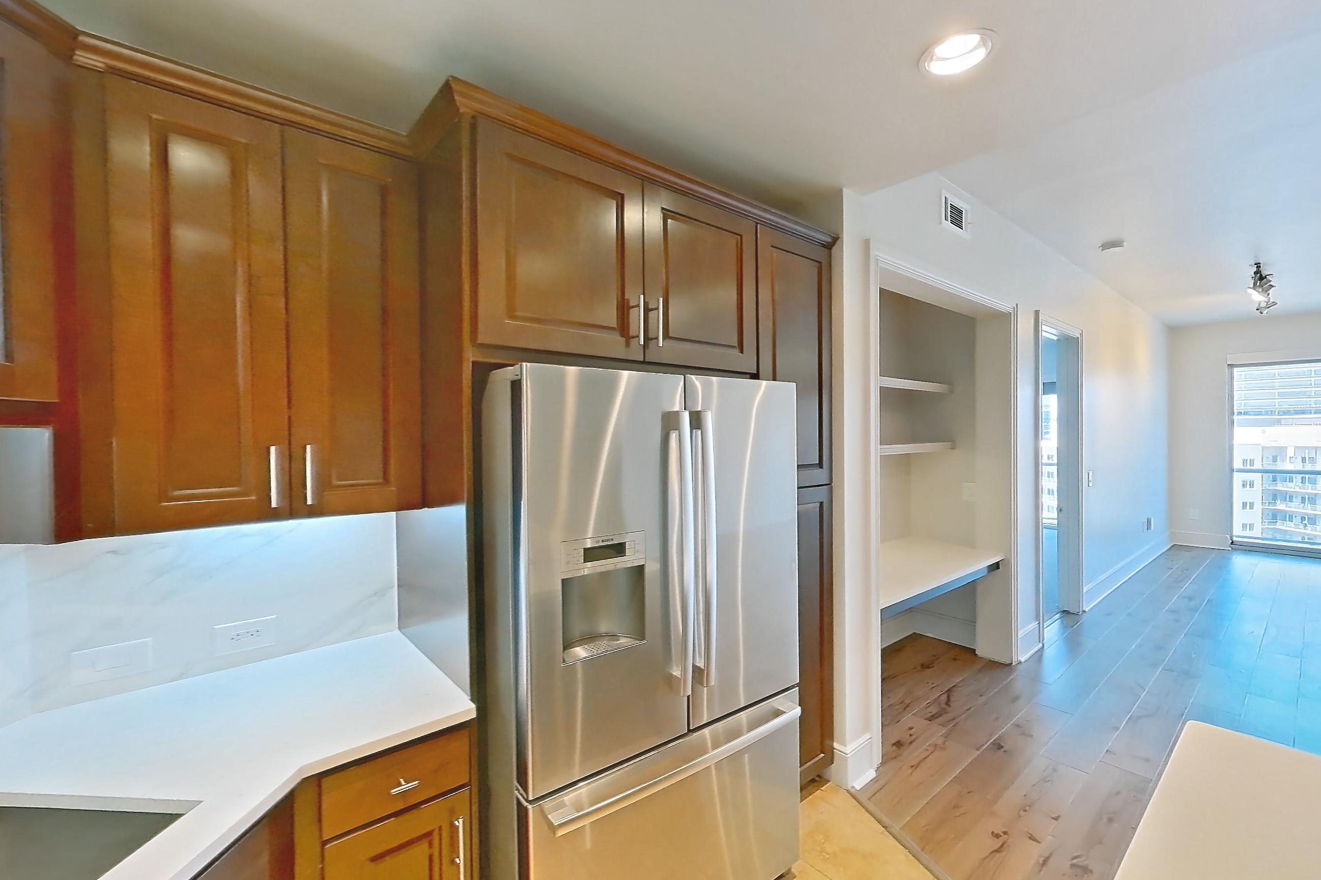 Kitchen with black appliances, cooktop, dishwasher, electric cooktop, light stone countertops, light tile flooring, microwave, oven/range, range hood, refrigerator, stainless steel appliances, and water & ice dispenser, Apartment 1809 at Cortland on McKinney