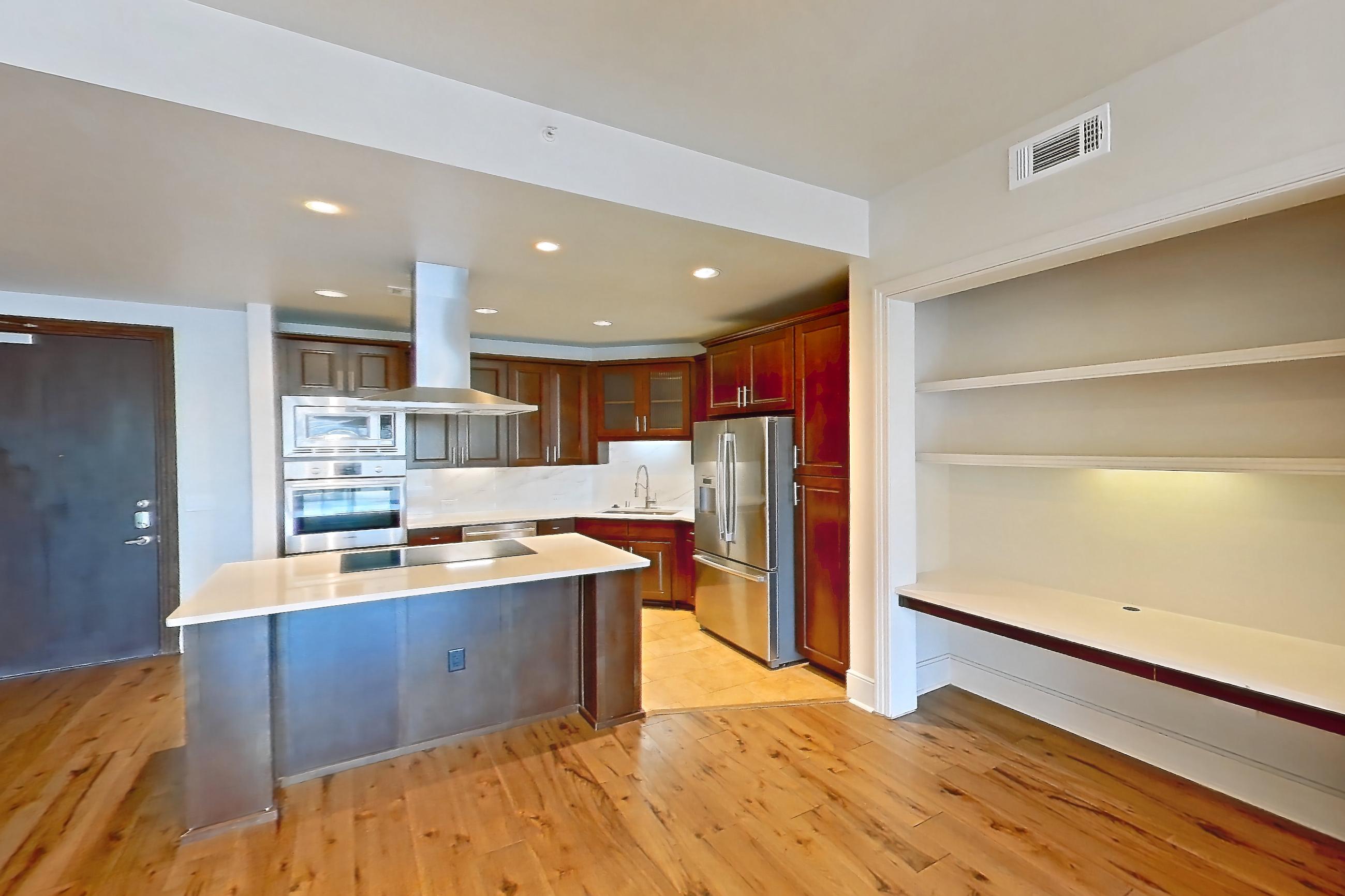 Living room with black appliances, cooktop, dishwasher, electric cooktop, kitchen island, light countertops, light stone countertops, light wood-finish flooring, oven/range, range hood, refrigerator, stainless steel appliances, and wood-finish flooring, Apartment 1809 at Cortland on McKinney