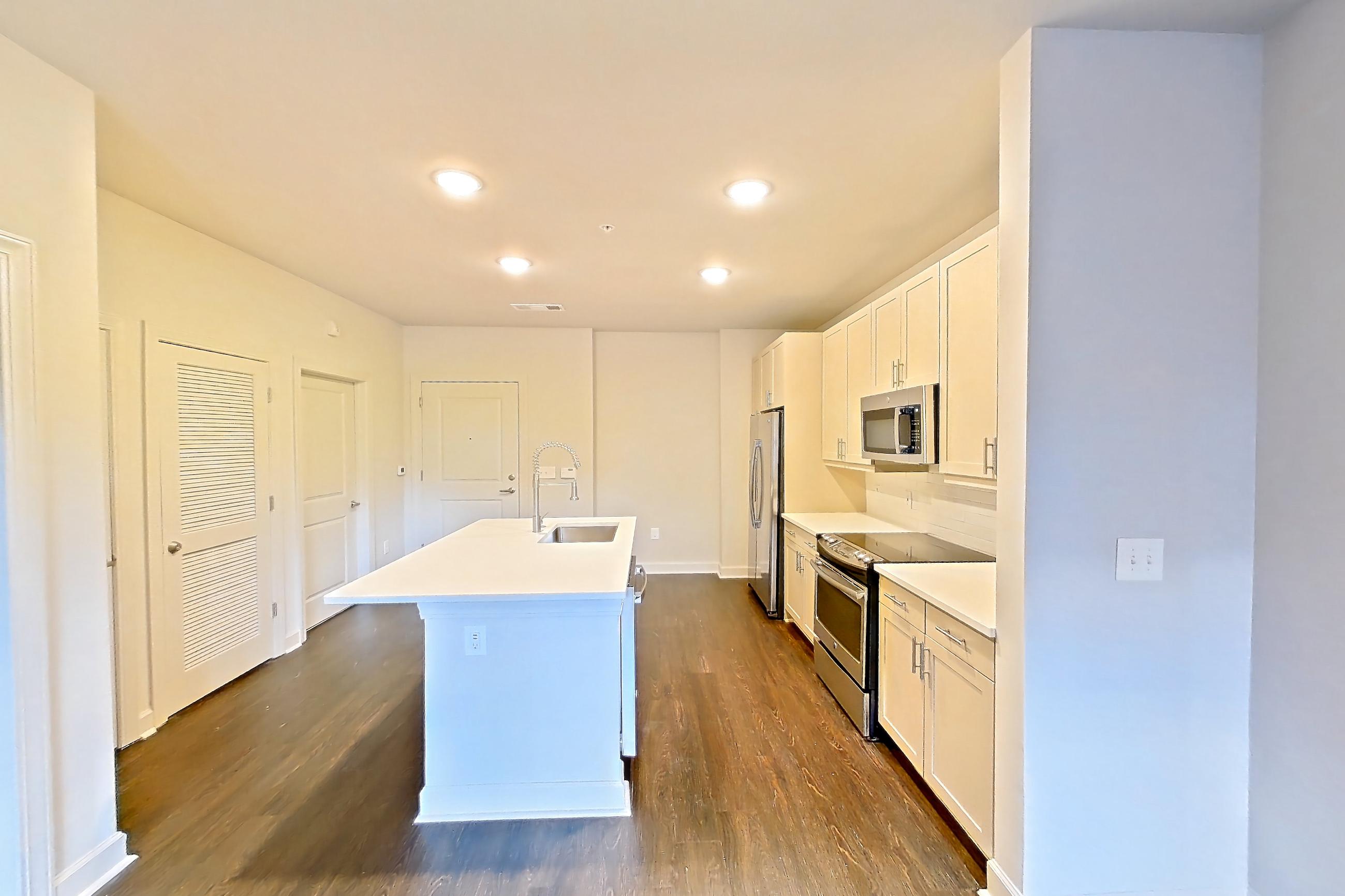 Living room with dark wood-finish flooring, electric range, kitchen island, light countertops, light stone countertops, microwave, oven/range, refrigerator, and stainless steel appliances, Apartment 1137 at Cortland Peachtree Battle