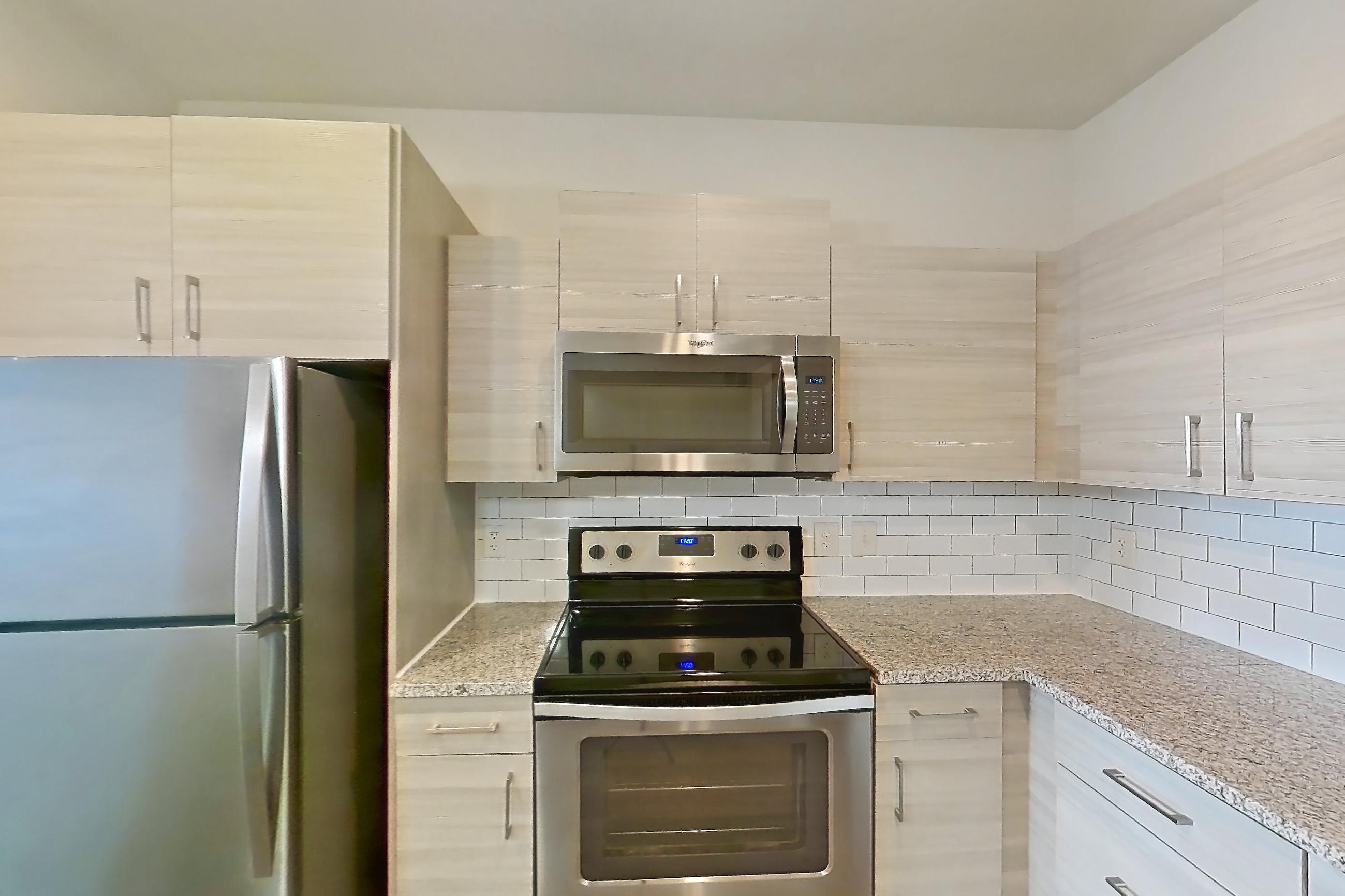 Kitchen with dark wood-finish flooring, dishwasher, electric range, light countertops, light stone countertops, oven/range, refrigerator, and stainless steel appliances, Apartment 144-301 at Domain
