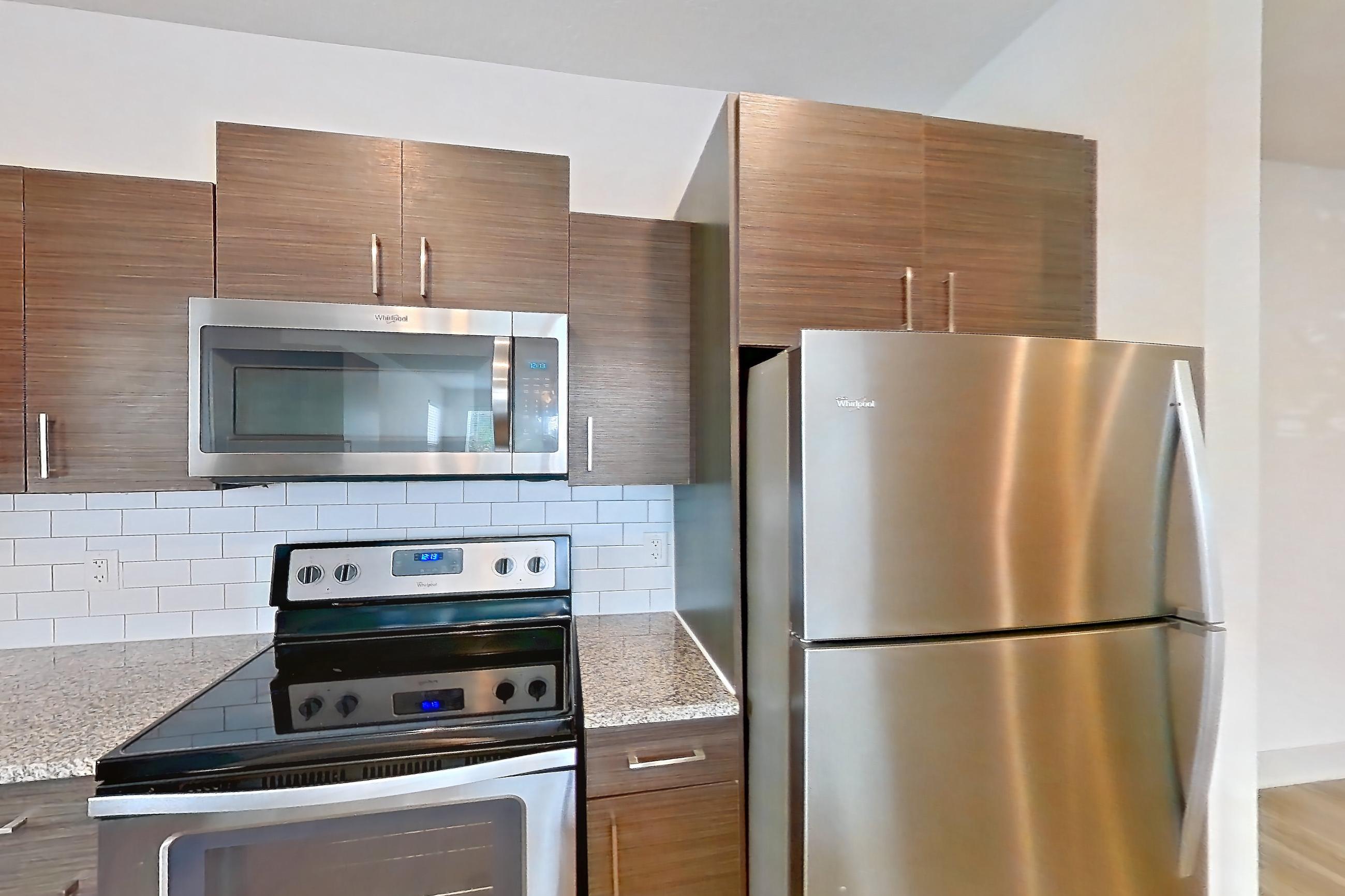 Kitchen with dishwasher, light stone countertops, light wood-finish flooring, oven/range, refrigerator, and stainless steel appliances, Apartment 156-101 at Domain